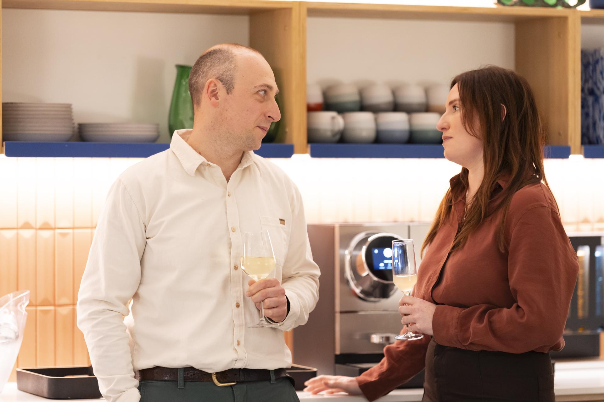 Two individuals engaged in conversation over drinks in a modern kitchen, highlighting technology's role in sustainable design discussions.