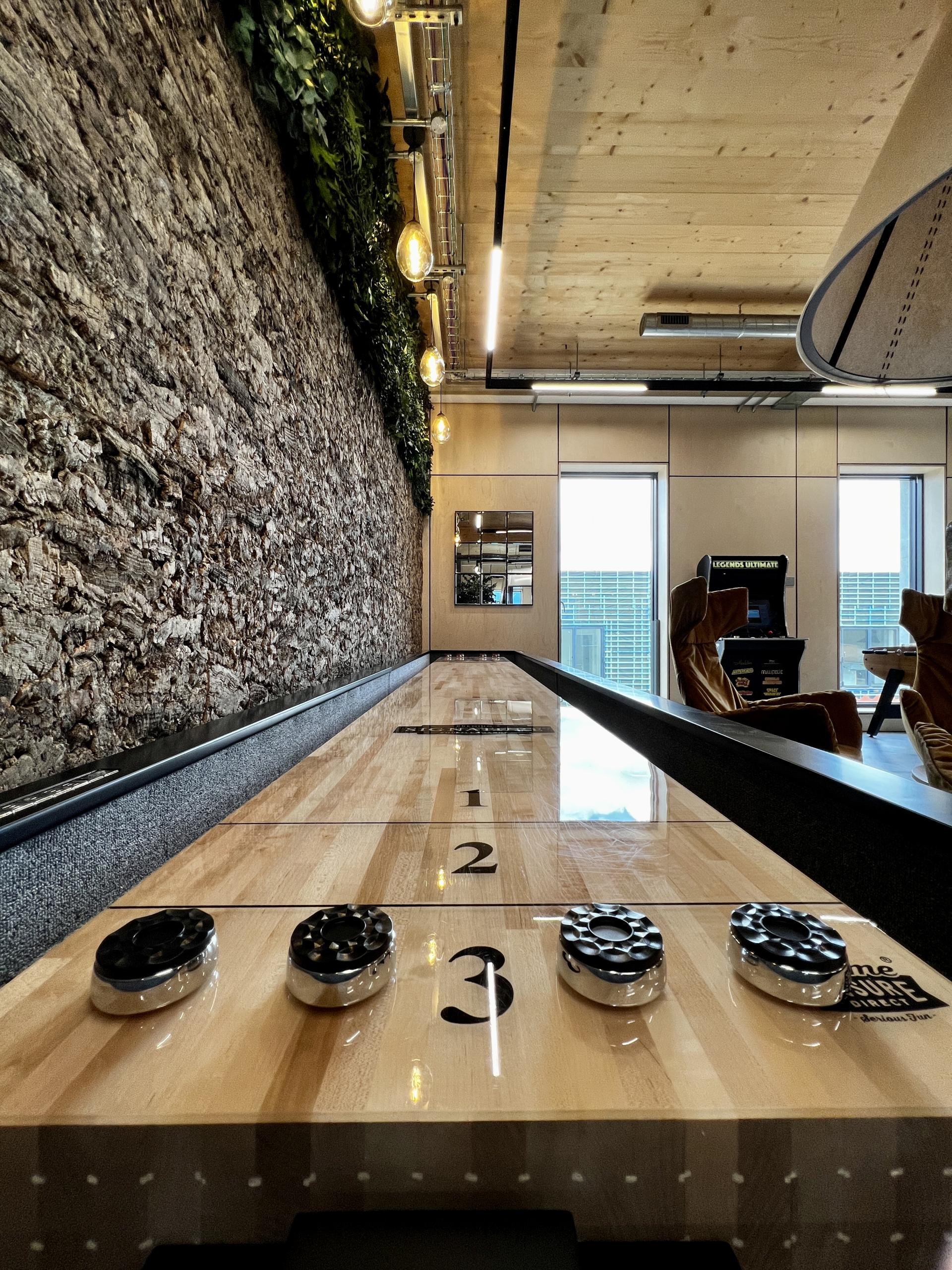 Modern workspace featuring a shuffleboard table, exposed brick wall, and sustainable design elements in Leeds' first net zero carbon office.