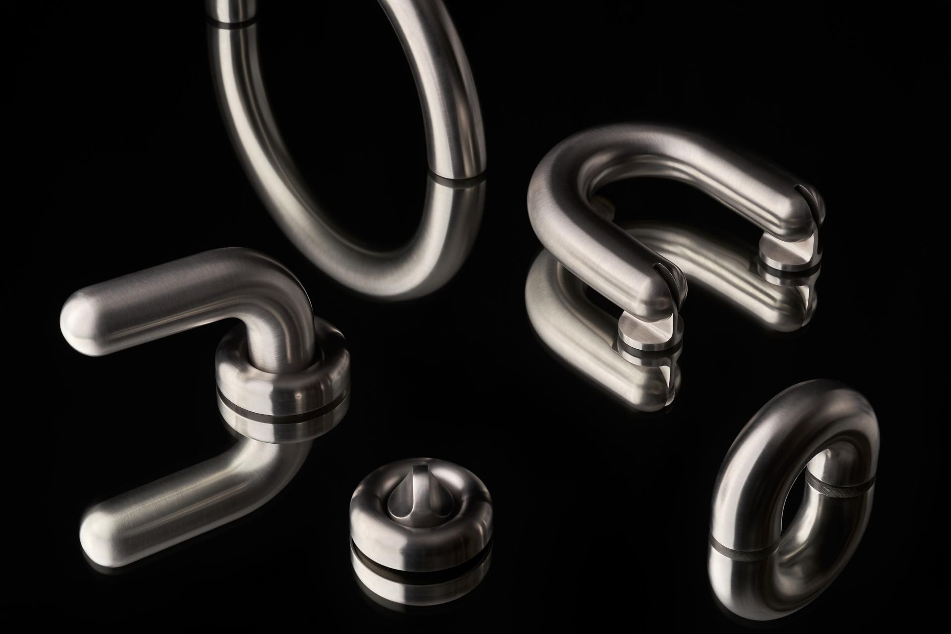 Stylish architectural ironmongery pieces from Tom Dixon’s FAT collection, showcasing sleek stainless steel design on a reflective surface.