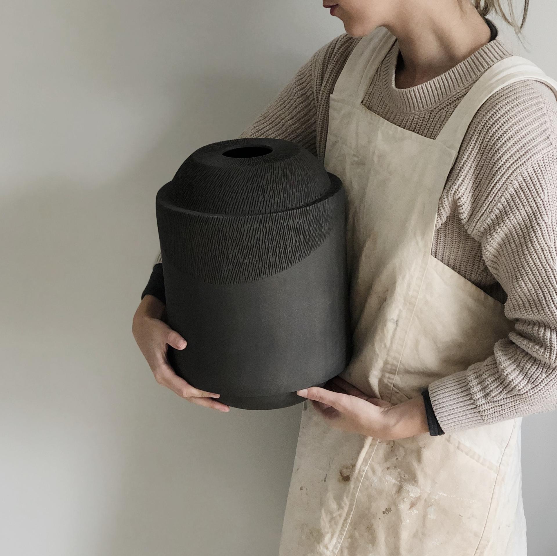 Sophie Farrar holding a large, textured black ceramic piece, showcasing her craftsmanship as a Sheffield-based ceramic artist.