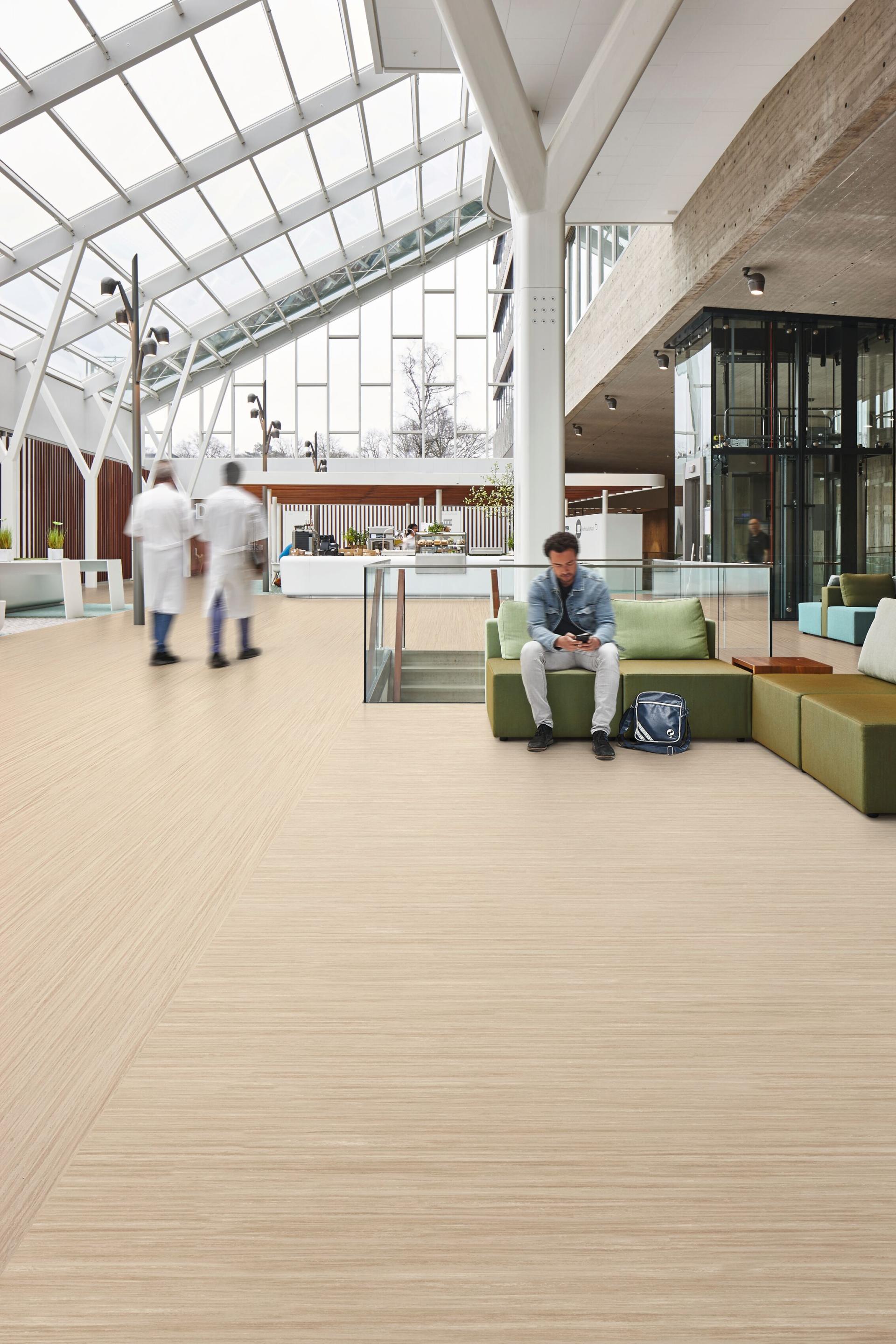 Modern indoor space featuring Forbo's Marmoleum Linear flooring, with a man sitting on a stylish lounge sofa.