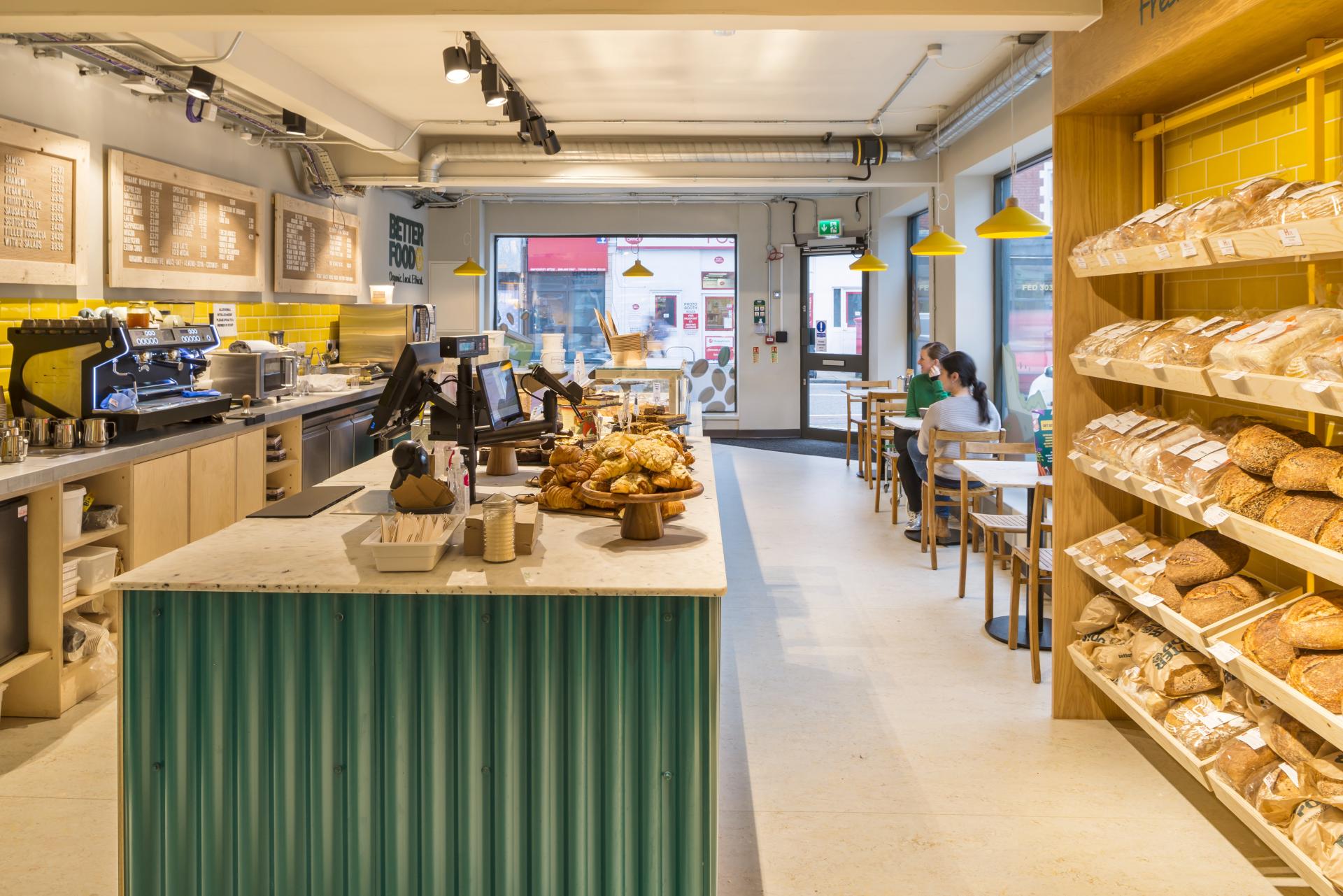 Bright, modern café-deli featuring baked goods, a coffee counter, and seating at Better Food's new Gloucester Road store.