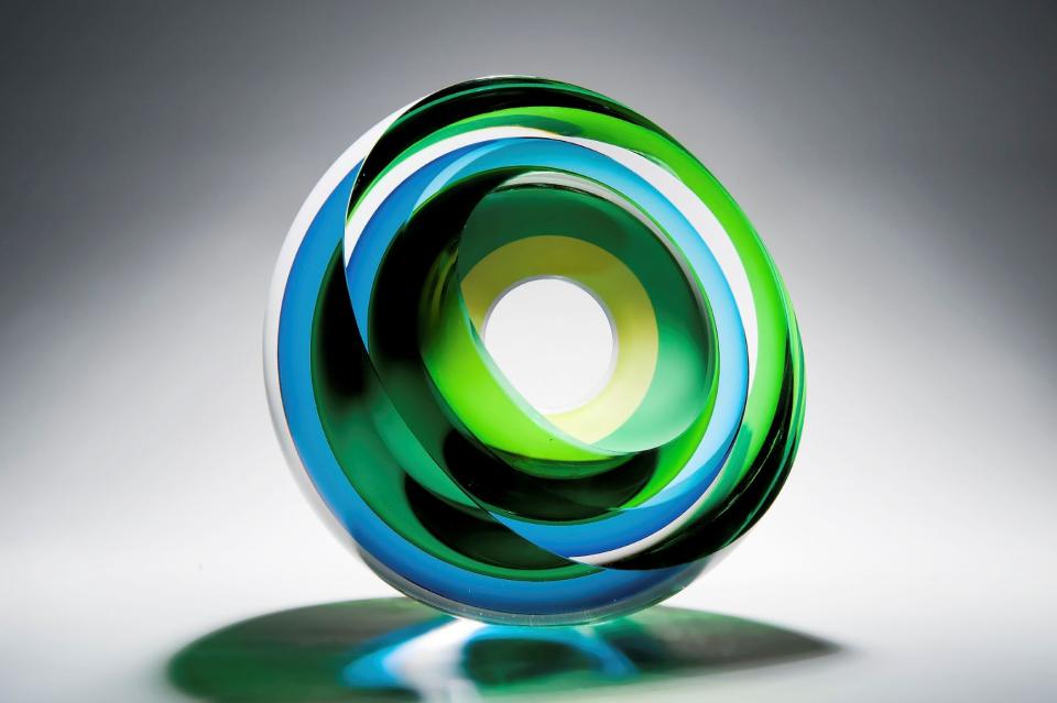 Colorful glass sculpture by Tim Rawlinson, showcasing swirling green and blue patterns with an artistic circular design.