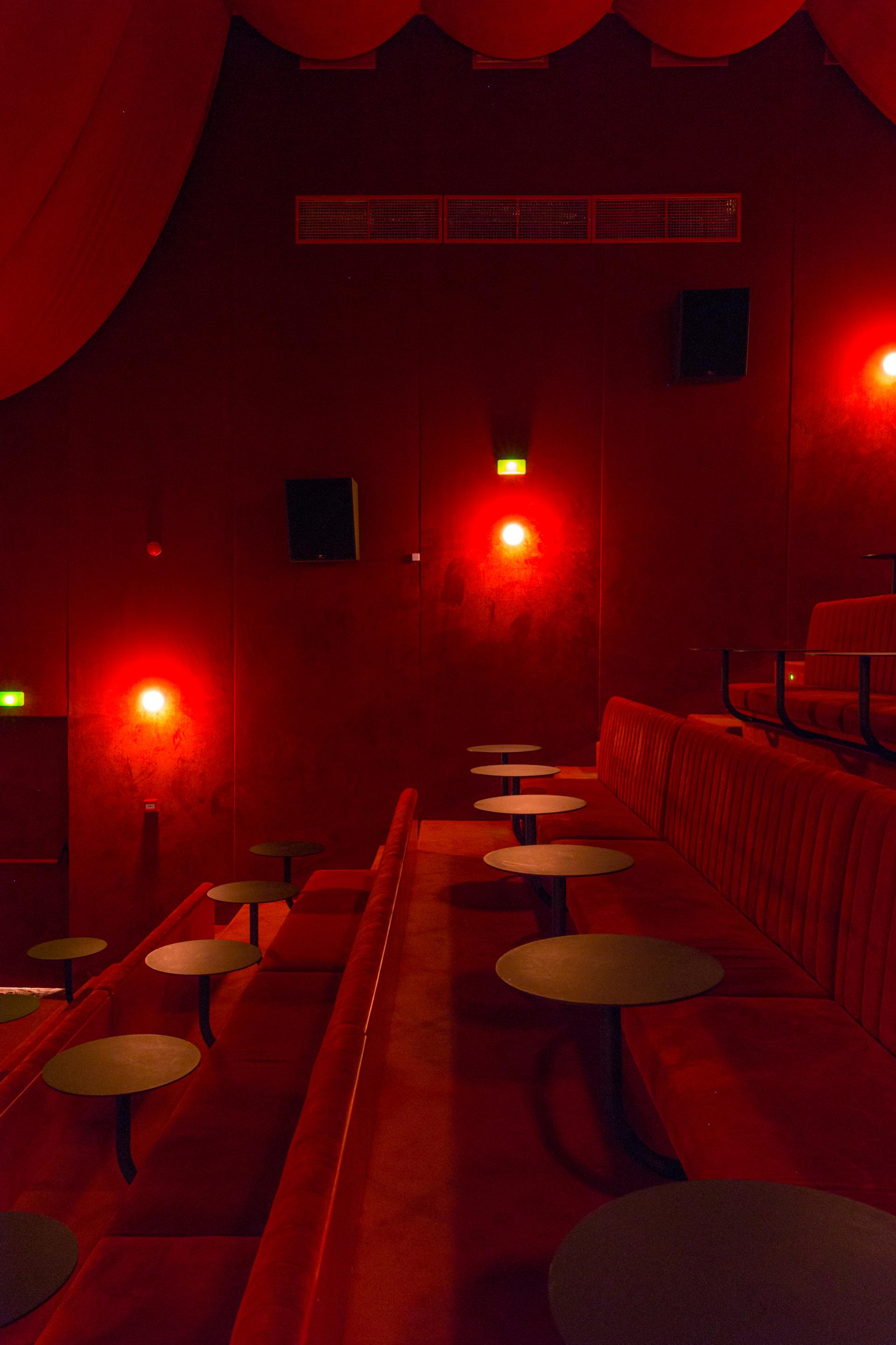 Vintage-inspired red cinema seating with small tables, creating an intimate atmosphere for enjoying films in Madrid.