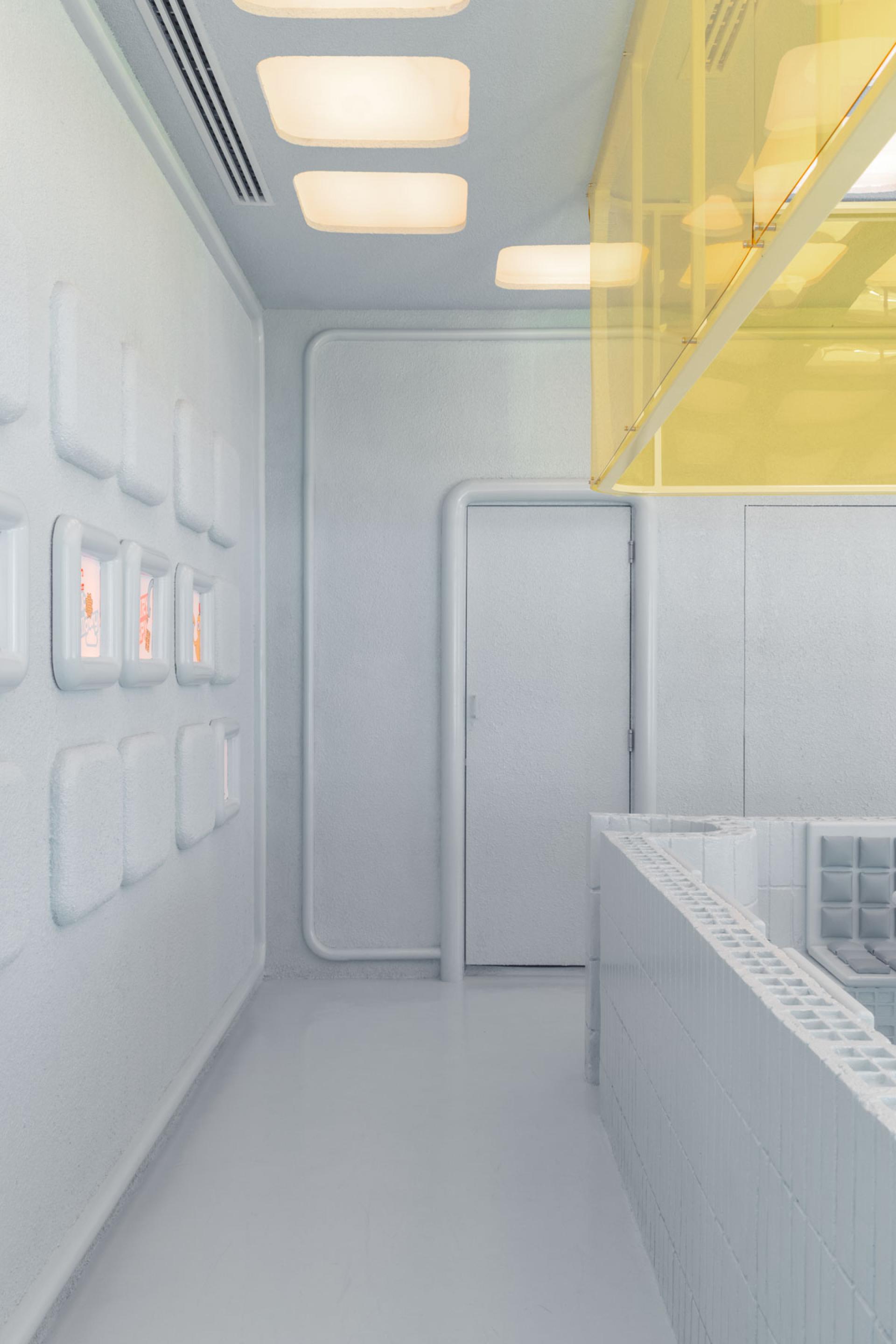 Futuristic interior design of Novu Waffle, featuring light-colored walls, geometric shapes, and a vibrant yellow lighting fixture.