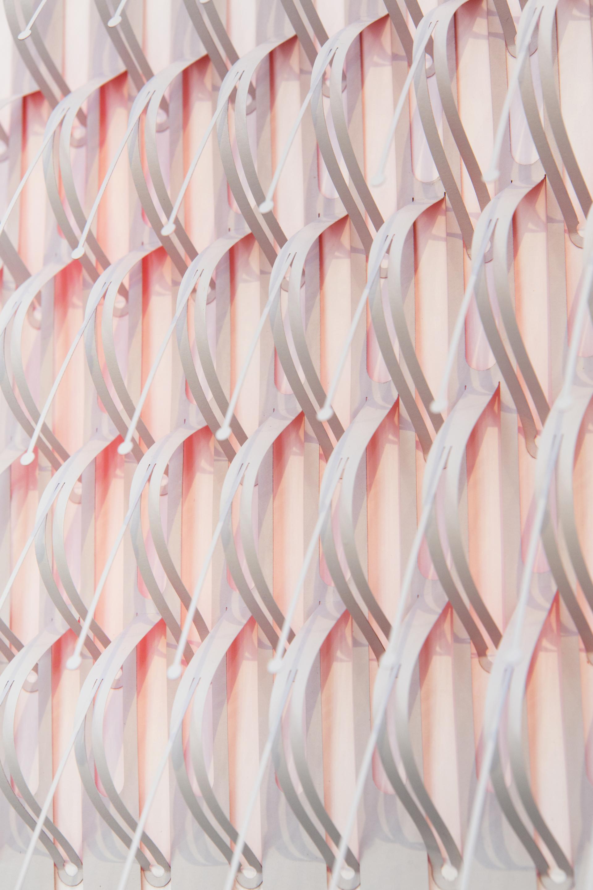Intricate wall installation featuring layered, curved strips in soft pink and gray, creating a serene visual effect.