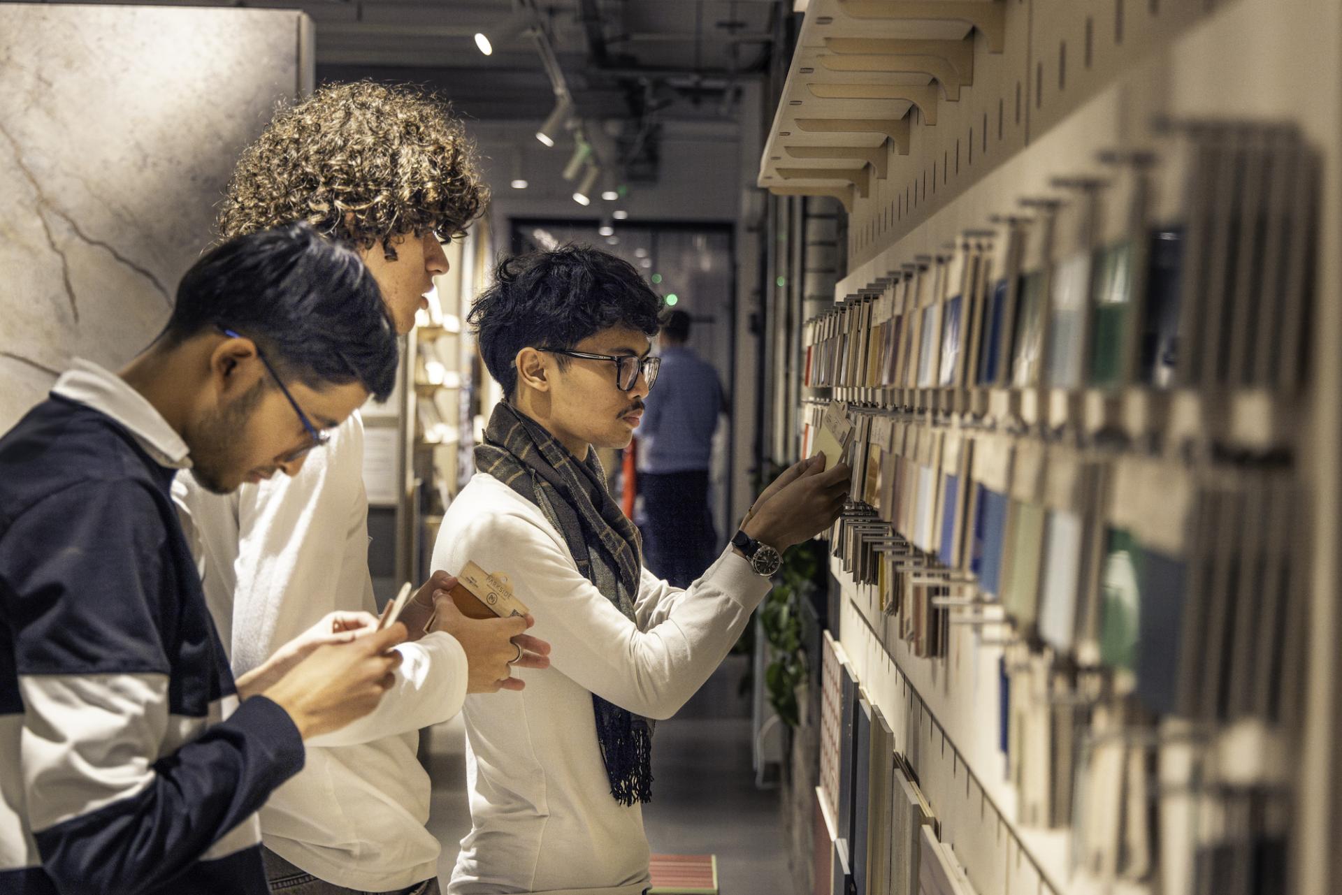 Three young professionals explore a modern office space, interacting with technology and design samples while embracing workplace innovation.