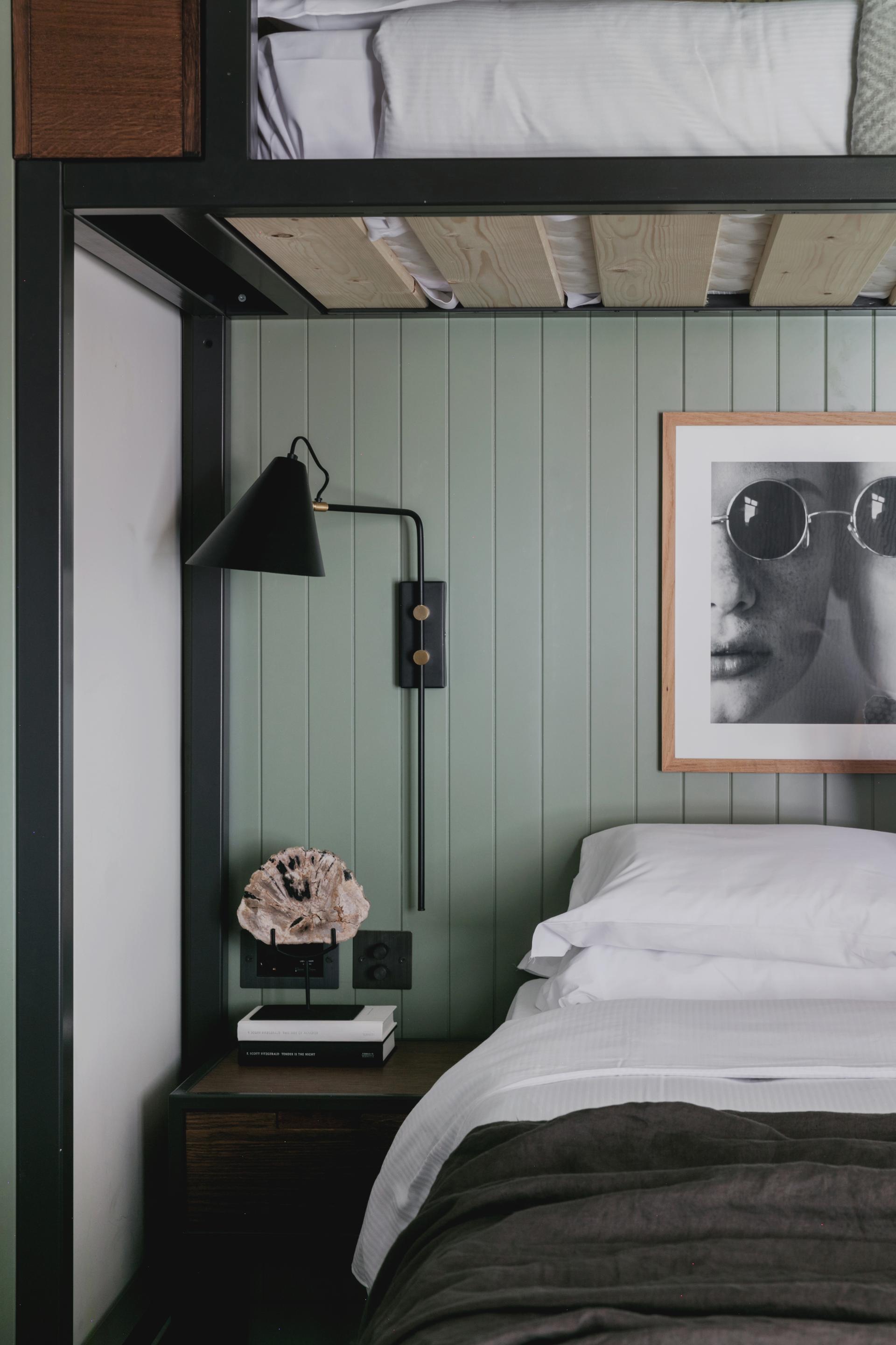 Stylishly designed hotel room with green paneling, modern lamp, artwork, and luxurious bedding, reflecting sustainable design principles.