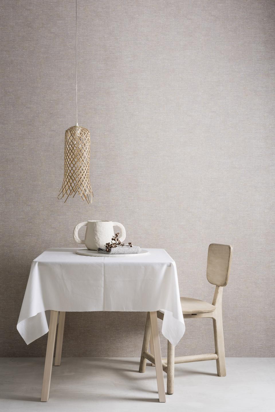 A stylish dining setup featuring Tektura Wallcoverings, a woven pendant lamp, minimalist table, and decorative ceramics.