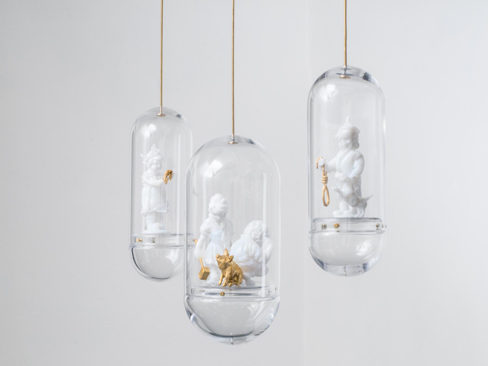 Hanging glass displays featuring intricate white and gold figurines, showcasing innovative glass design at the London Design Fair.
