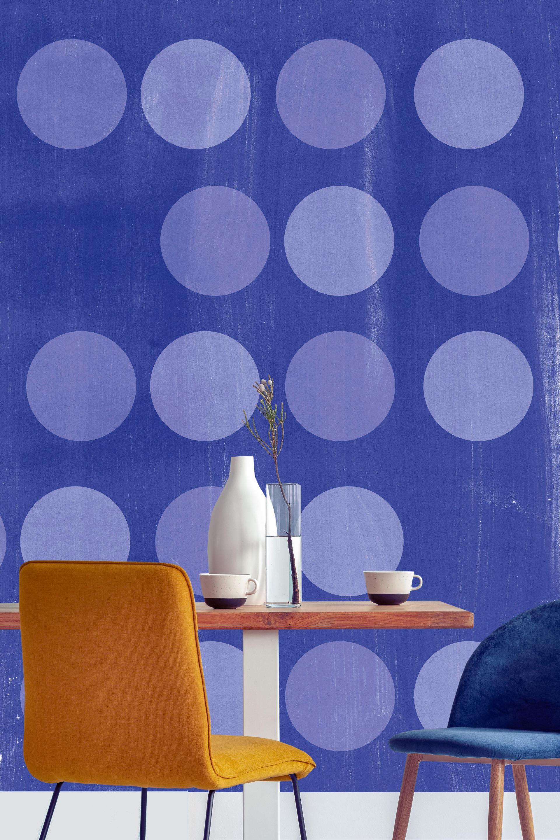 Bold blue wallcovering featuring large circles, with a wooden table set and colorful chairs, enhancing commercial interior design.