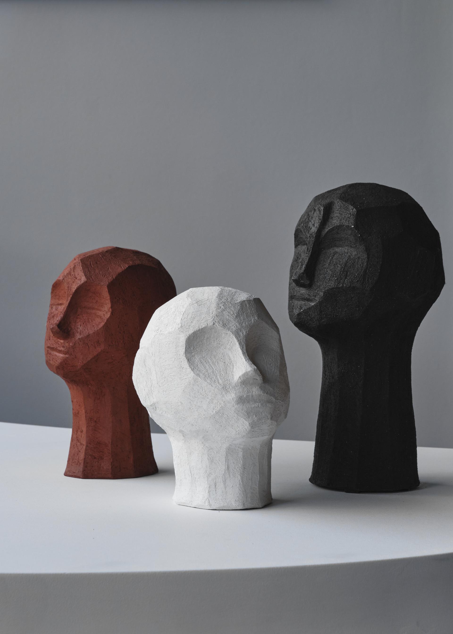 Three abstract sculptures resembling stylized human heads in red, white, and black, displayed on a round table.