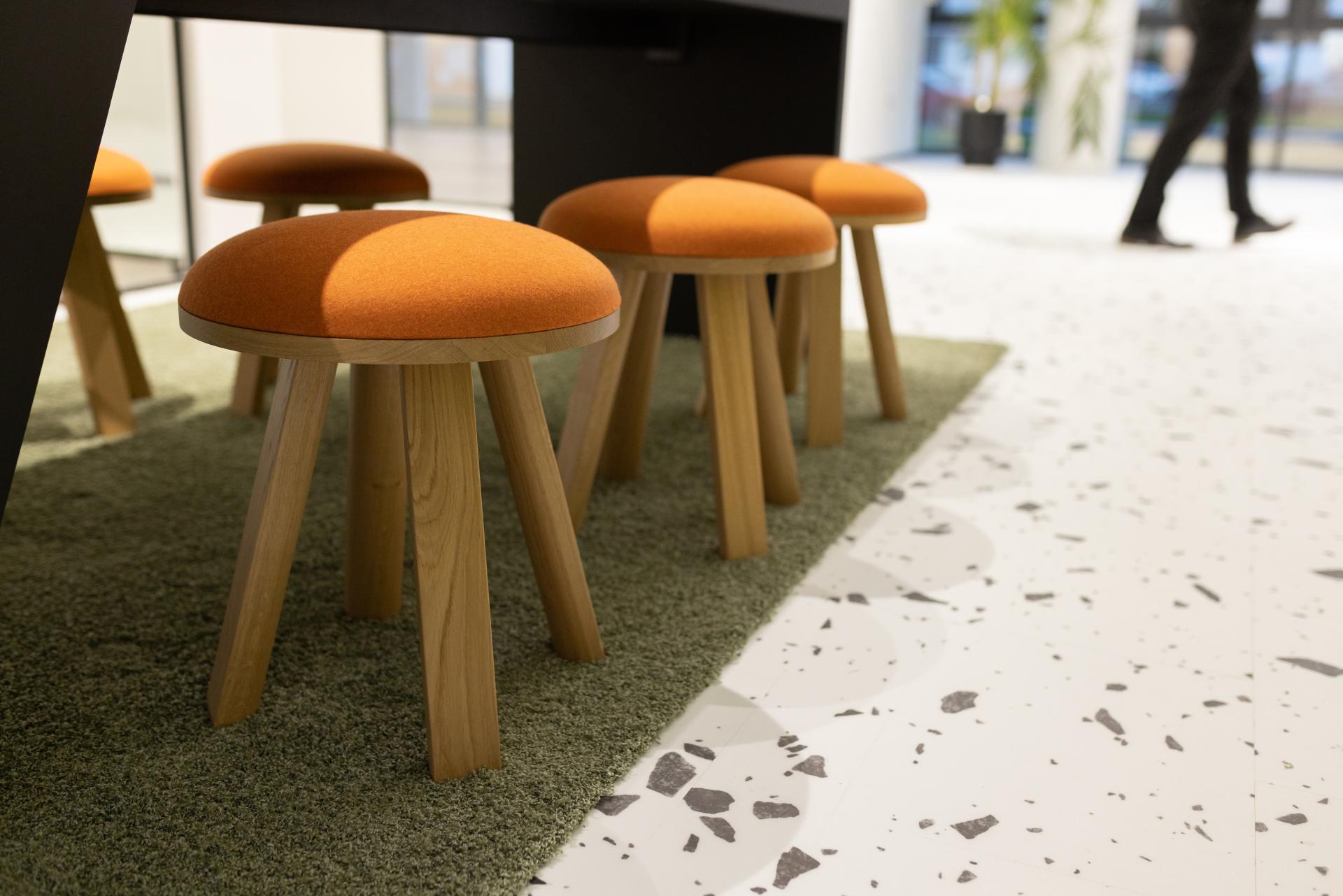 Modern interior featuring orange upholstered stools on a green rug, set against bold terrazzo flooring in a biophilic design space.