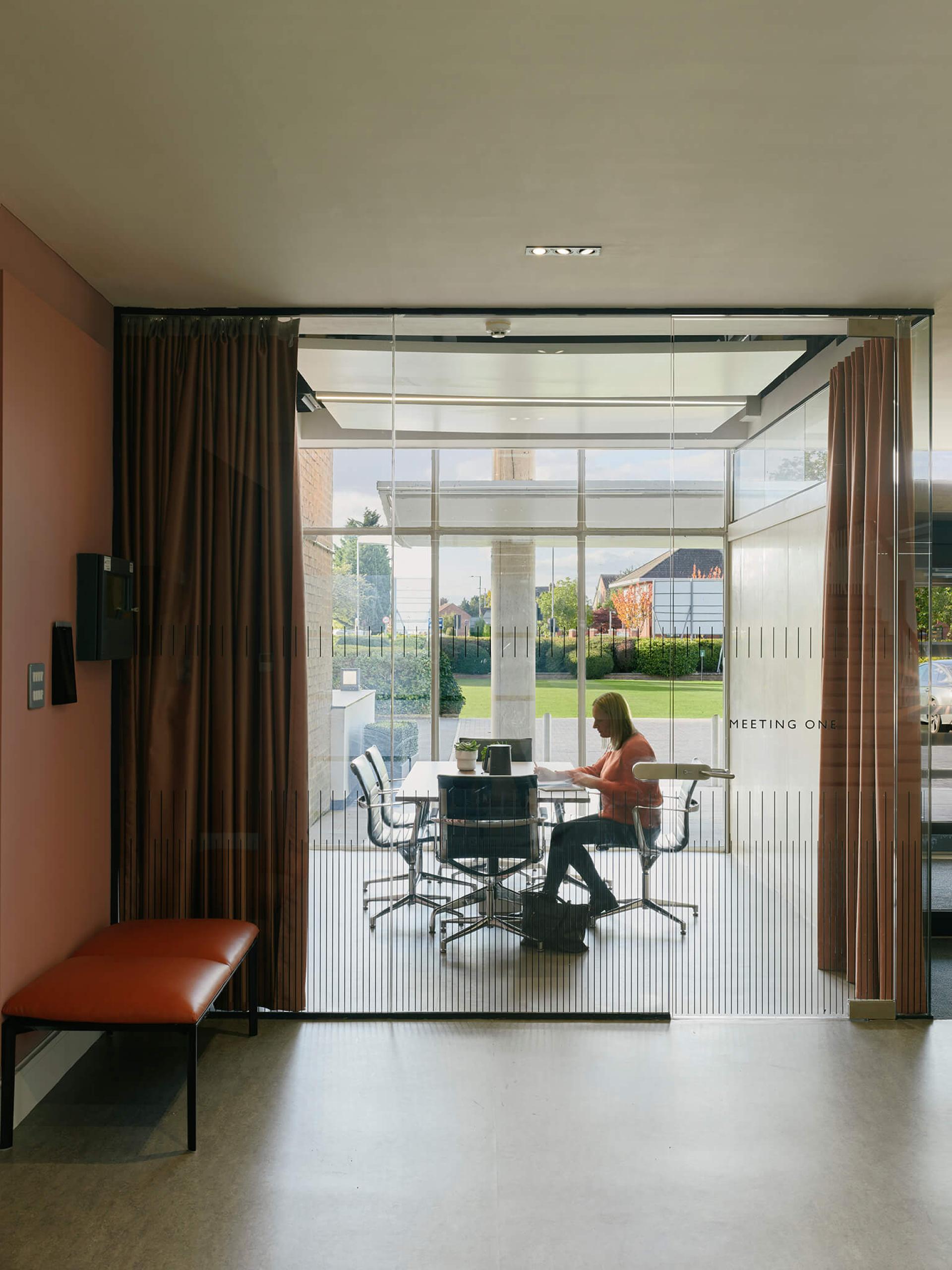 Modern office interior featuring a woman working at a glass meeting room in Manchester International Office Centre.