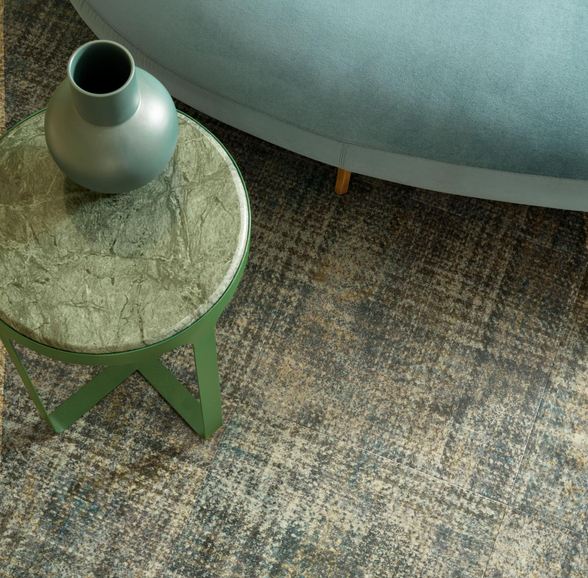 Elegant green table with a vase atop a textured floor featuring Forbo’s Allura Decibel Luxury Vinyl Tile collection.