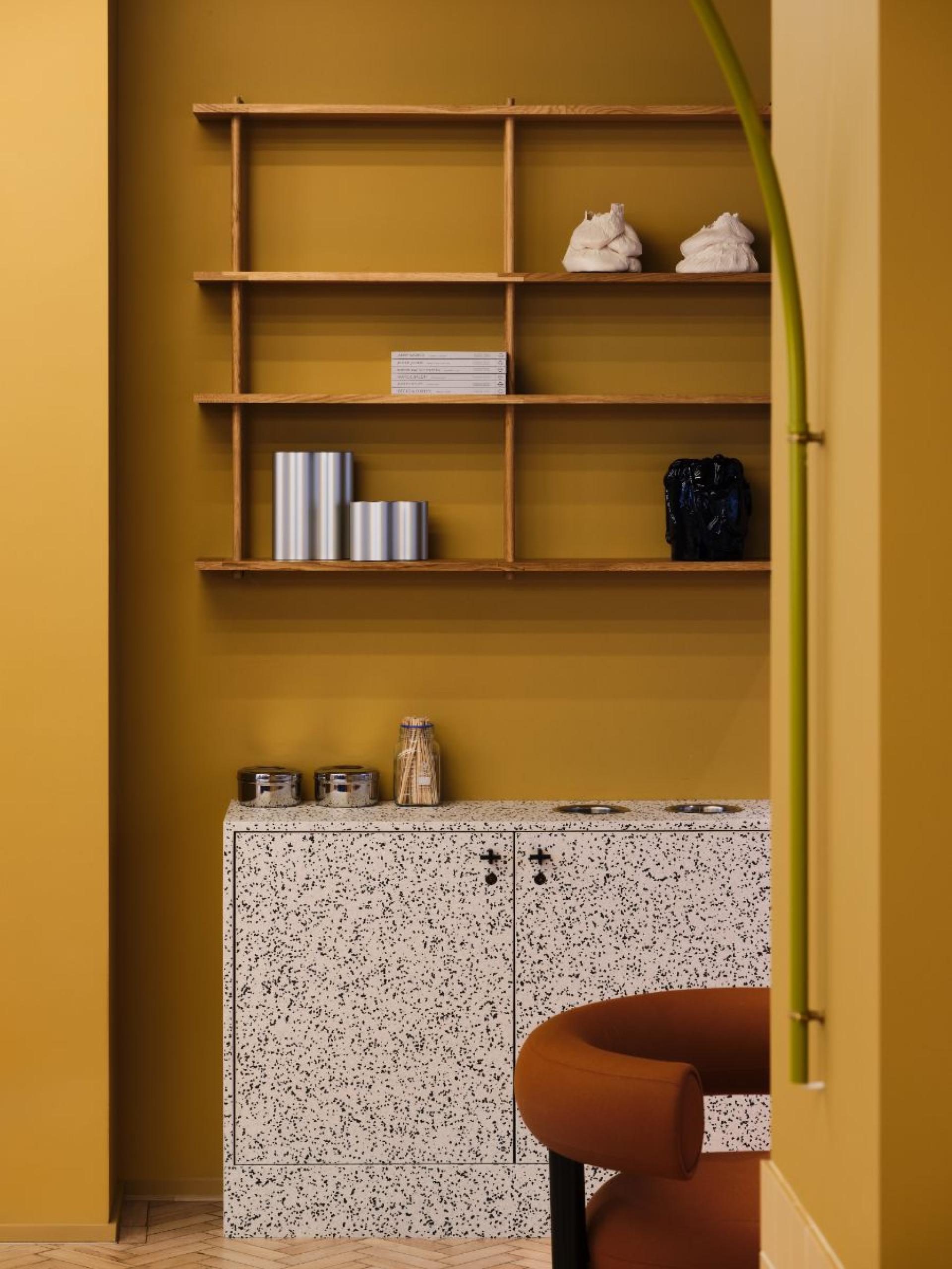 Stylish flexible workspace featuring a speckled cabinet, wooden shelves, and a cozy seating area with amber tones.