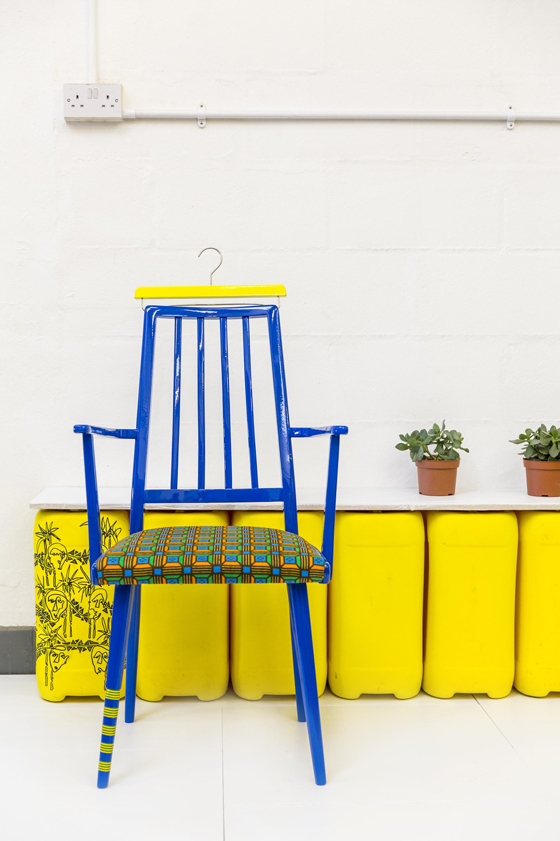 Vibrant blue and yellow chair with patterned upholstery, showcasing Yinka Ilori's upcycled design style against a minimalist background.
