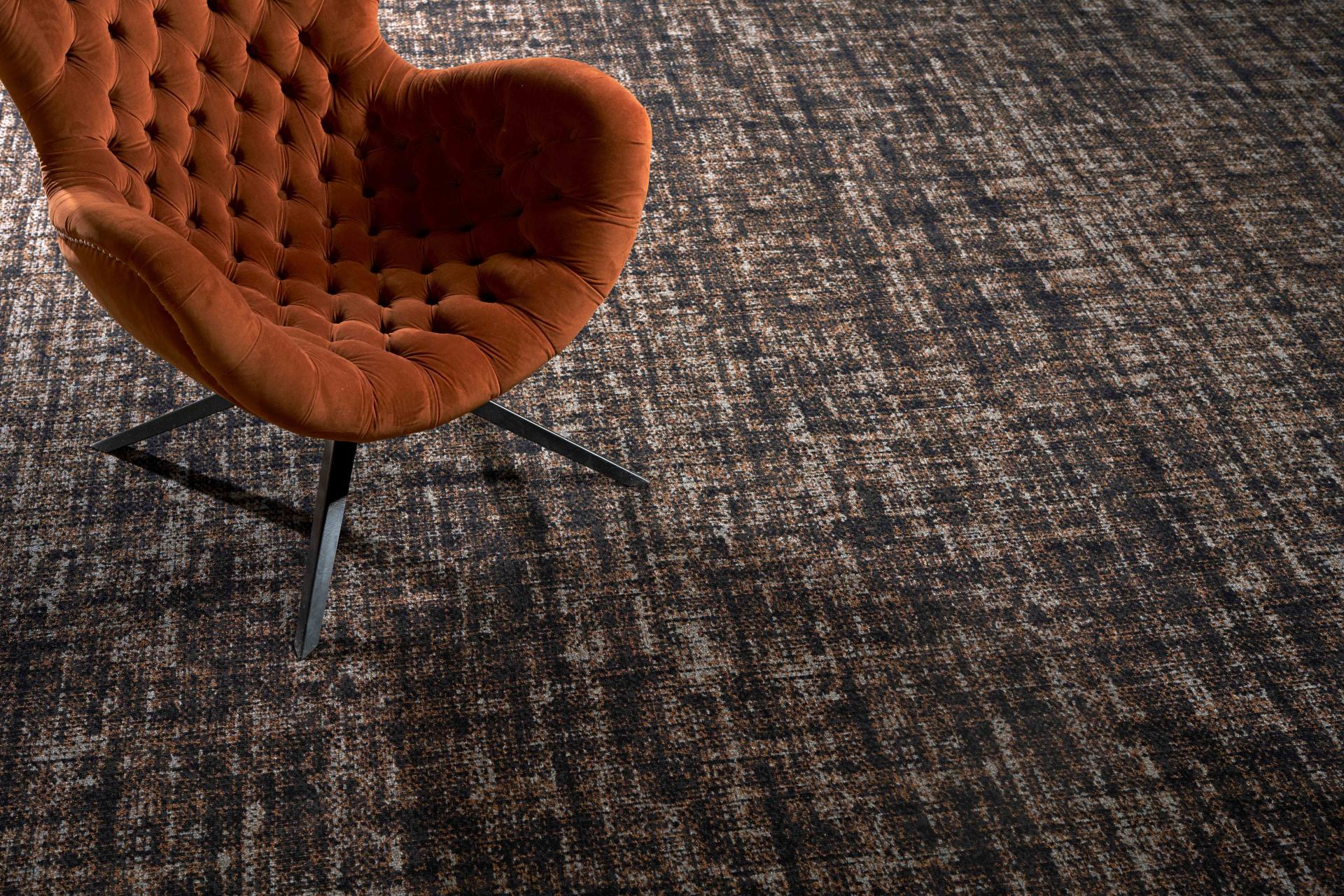 Stylish orange tufted chair on a textured Patina carpet from Newhey Carpets, showcasing modern hospitality design.