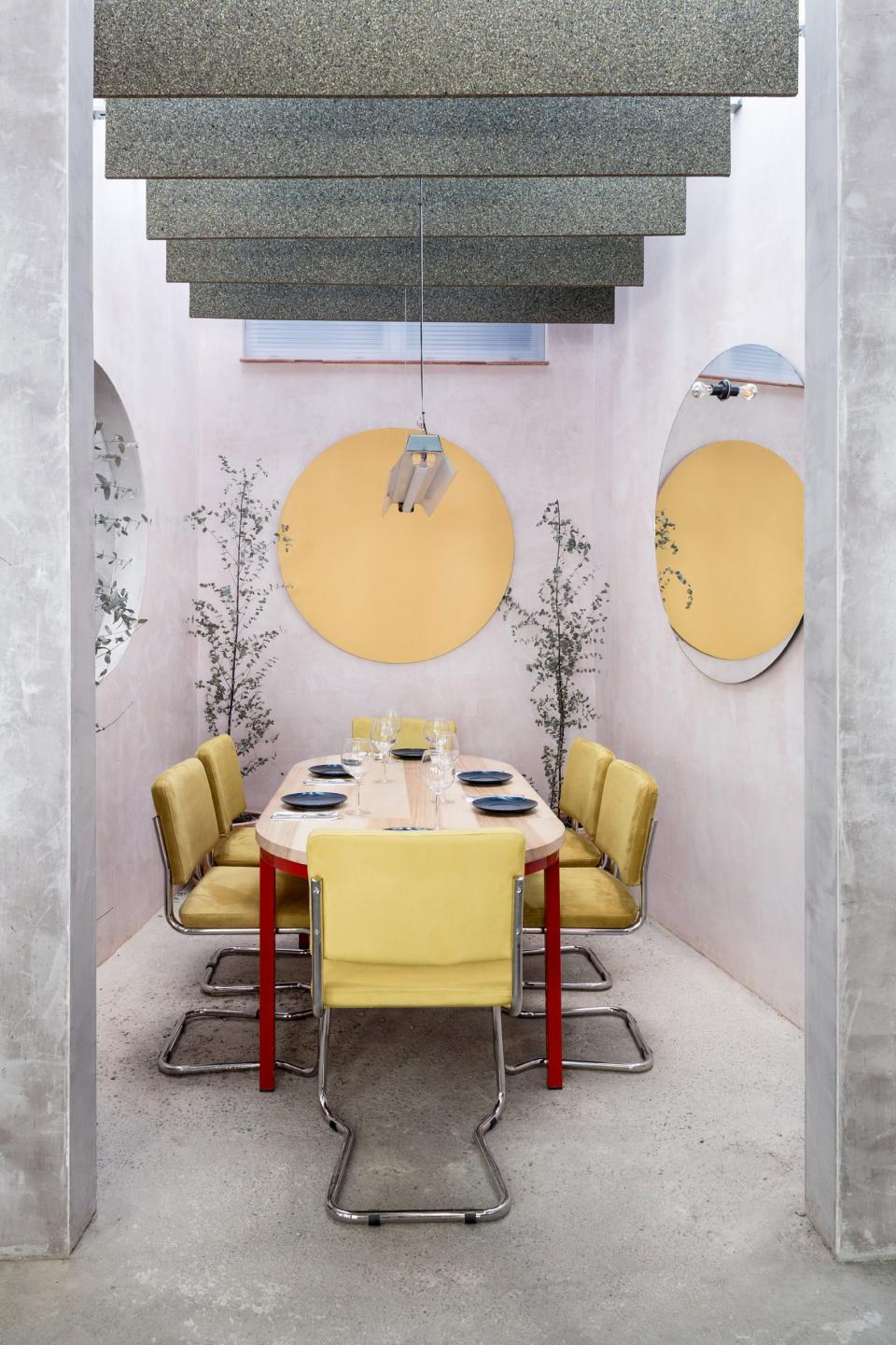 Interior design of a Seville restaurant featuring a concrete structure, pastel walls, yellow furniture, and unique lighting.