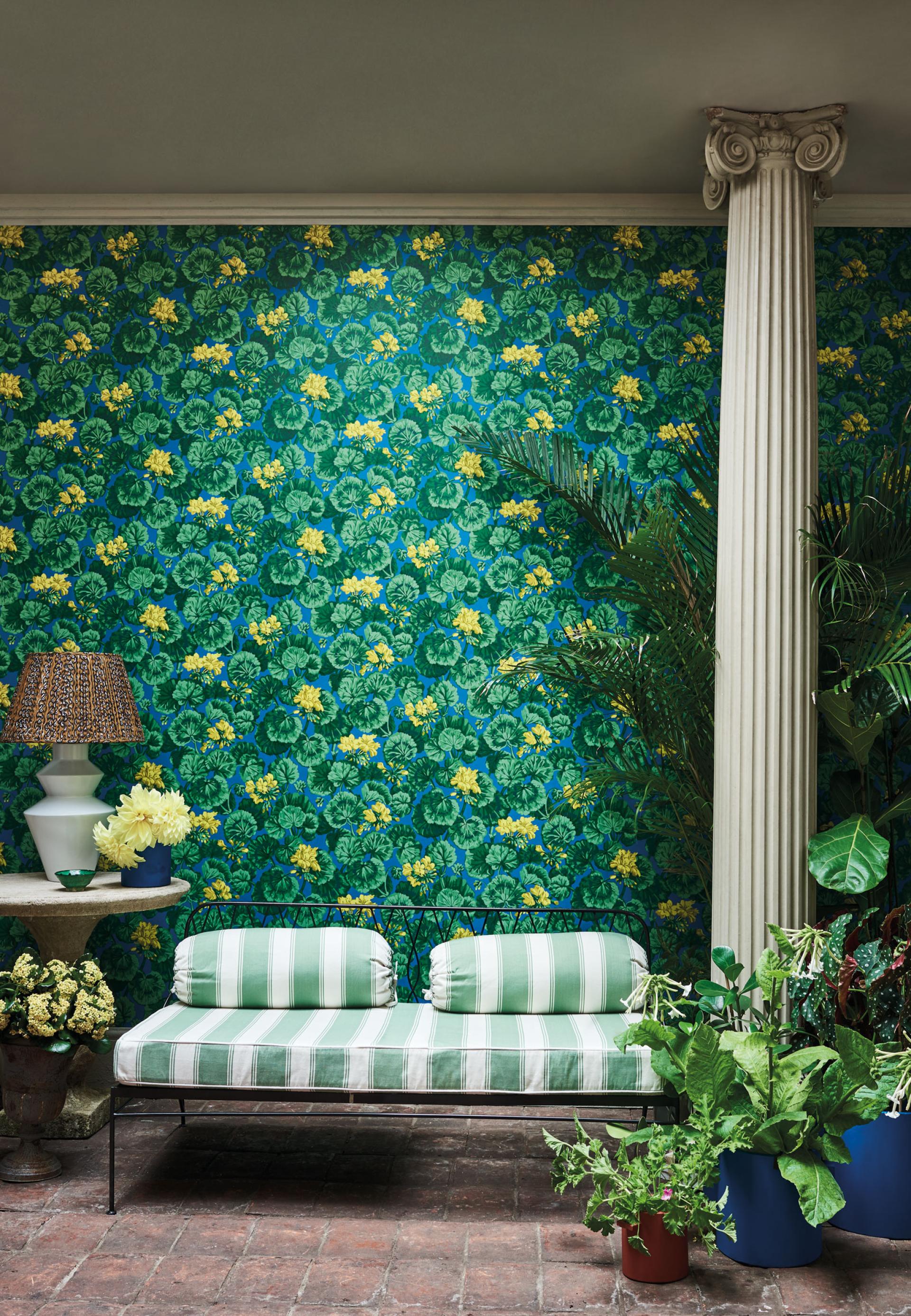Vibrant green botanical wallpaper with yellow flowers, complemented by a stylish sofa and decorative plants in a chic interior.