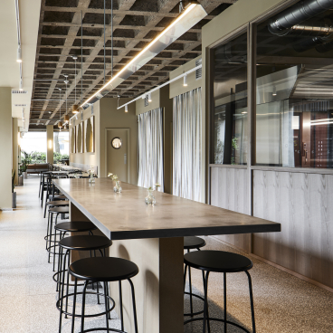 Modern patisserie interior featuring a long concrete table, minimalist black stools, and soft natural lighting.
