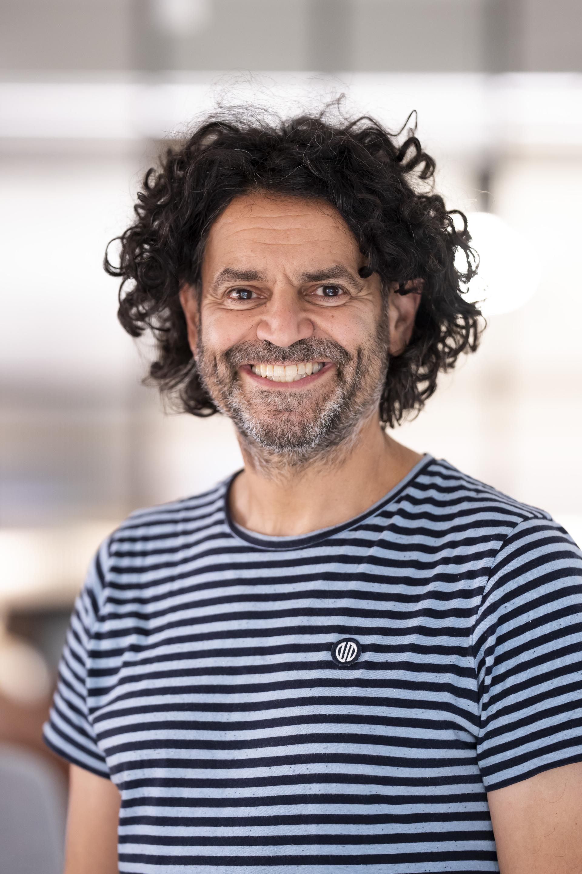 Middle-aged man with curly hair smiles warmly, reflecting the positive impact of data in the modern workplace setting.