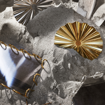 Decorative metal trays, including gold and silver, resting on sand, symbolizing the unique design elements for 13.10 Ristorante.