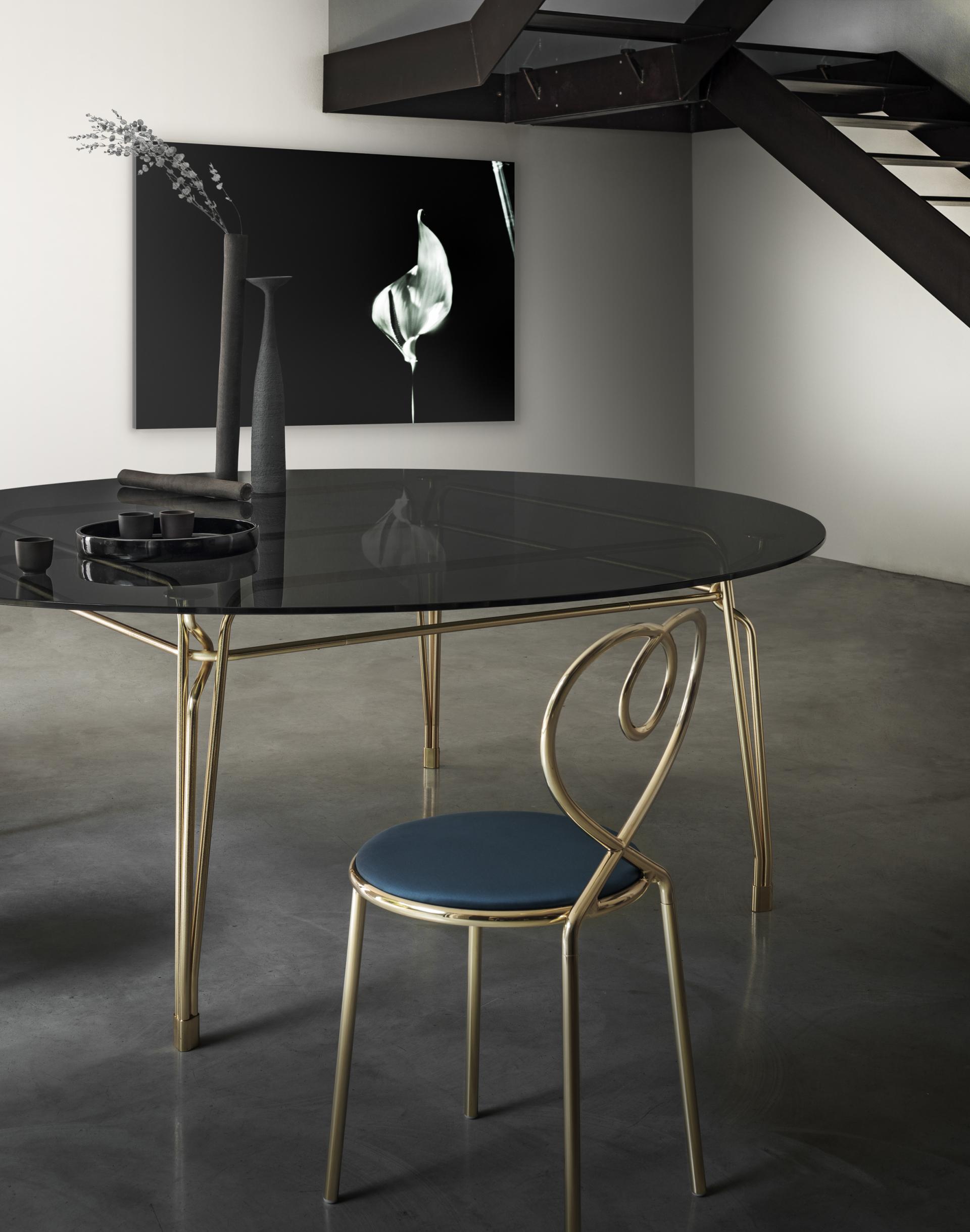 Elegant brass dining table with a glass top and unique chair design, showcasing GHIDINI1961's heritage in modern furniture.