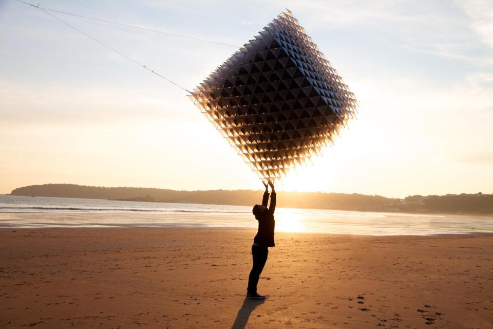 Person flying a geometric kite at sunset on a beach, showcasing innovative design and architecture principles.