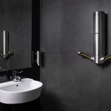 Dyson hand dryer mounted on a dark wall, alongside a sleek white sink in a modern restroom setting.