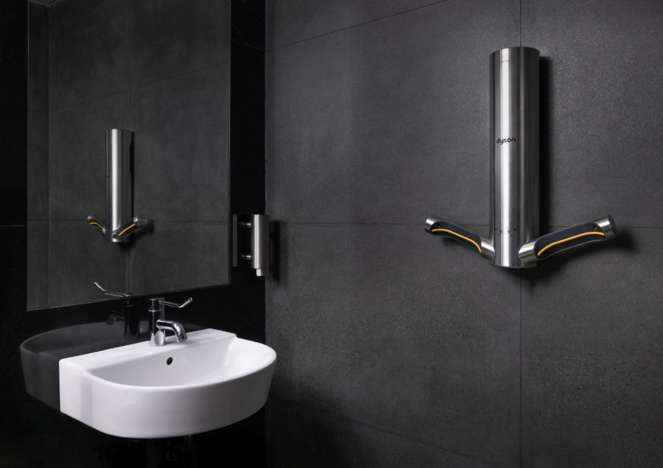Dyson hand dryer mounted on a dark wall, alongside a sleek white sink in a modern restroom setting.