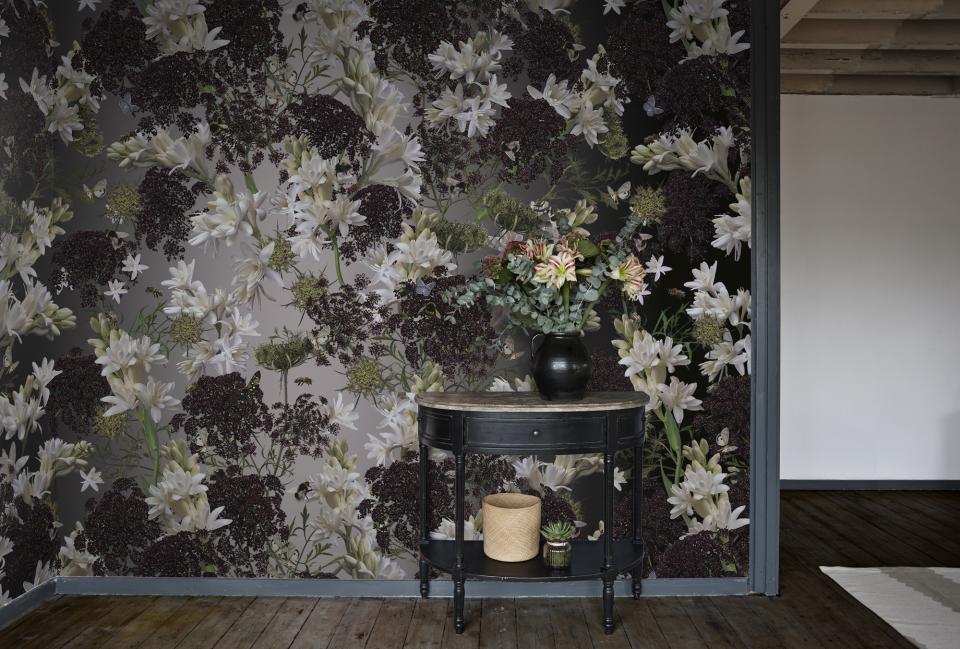 Dramatic floral wallpaper featuring white and dark flowers behind a stylish table with a flower arrangement.