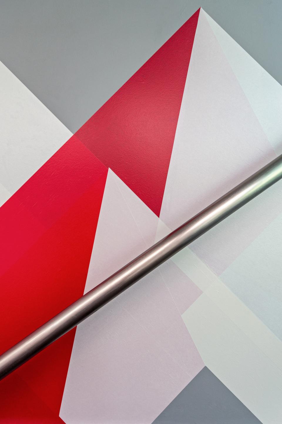 Colorful geometric wall design featuring bold red and white triangles with a sleek metallic bar across the image.