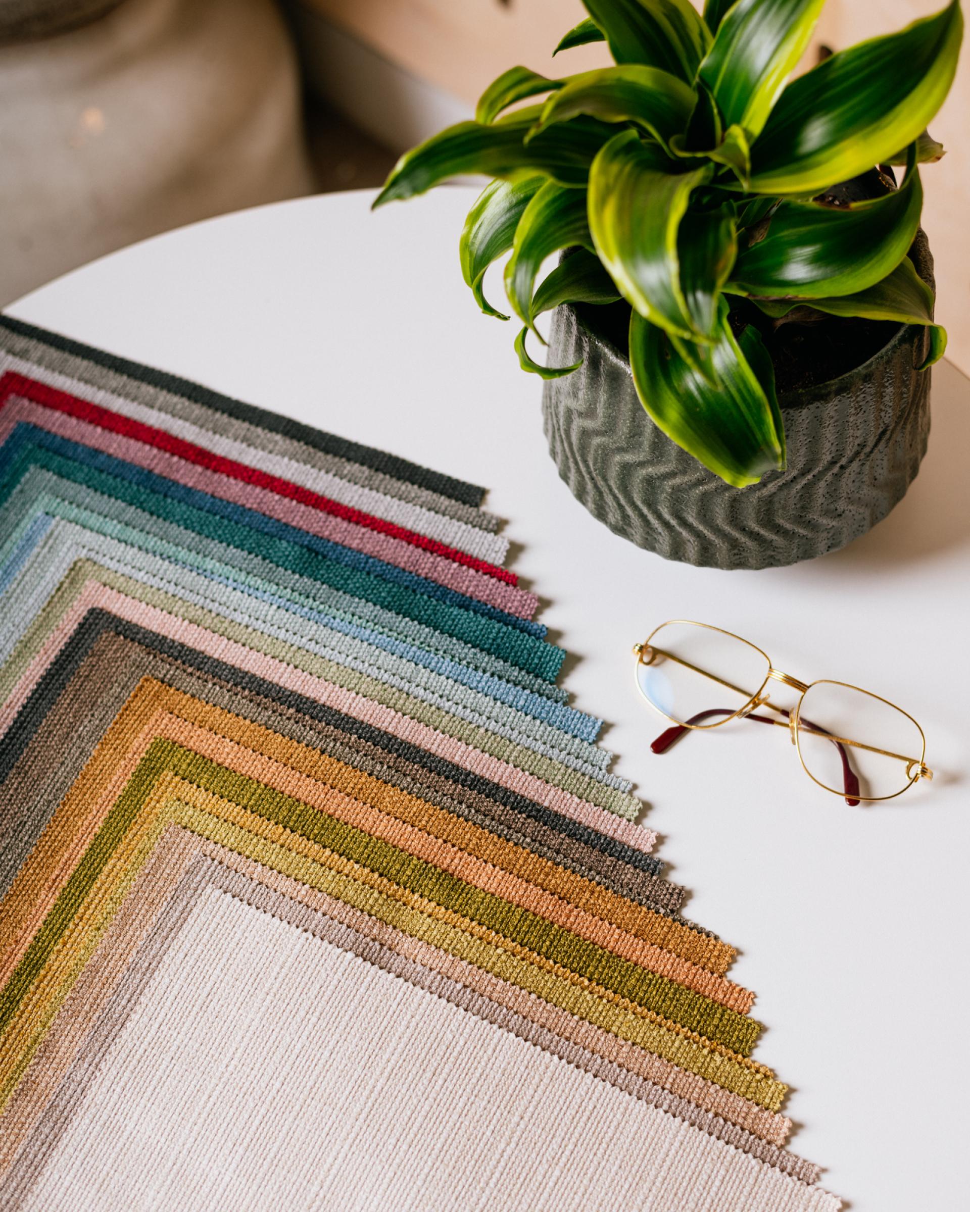 Vibrant upholstery fabric swatches in various colors alongside a plant and glasses, showcasing Agua Fabrics' Eden and Bouclé collections.