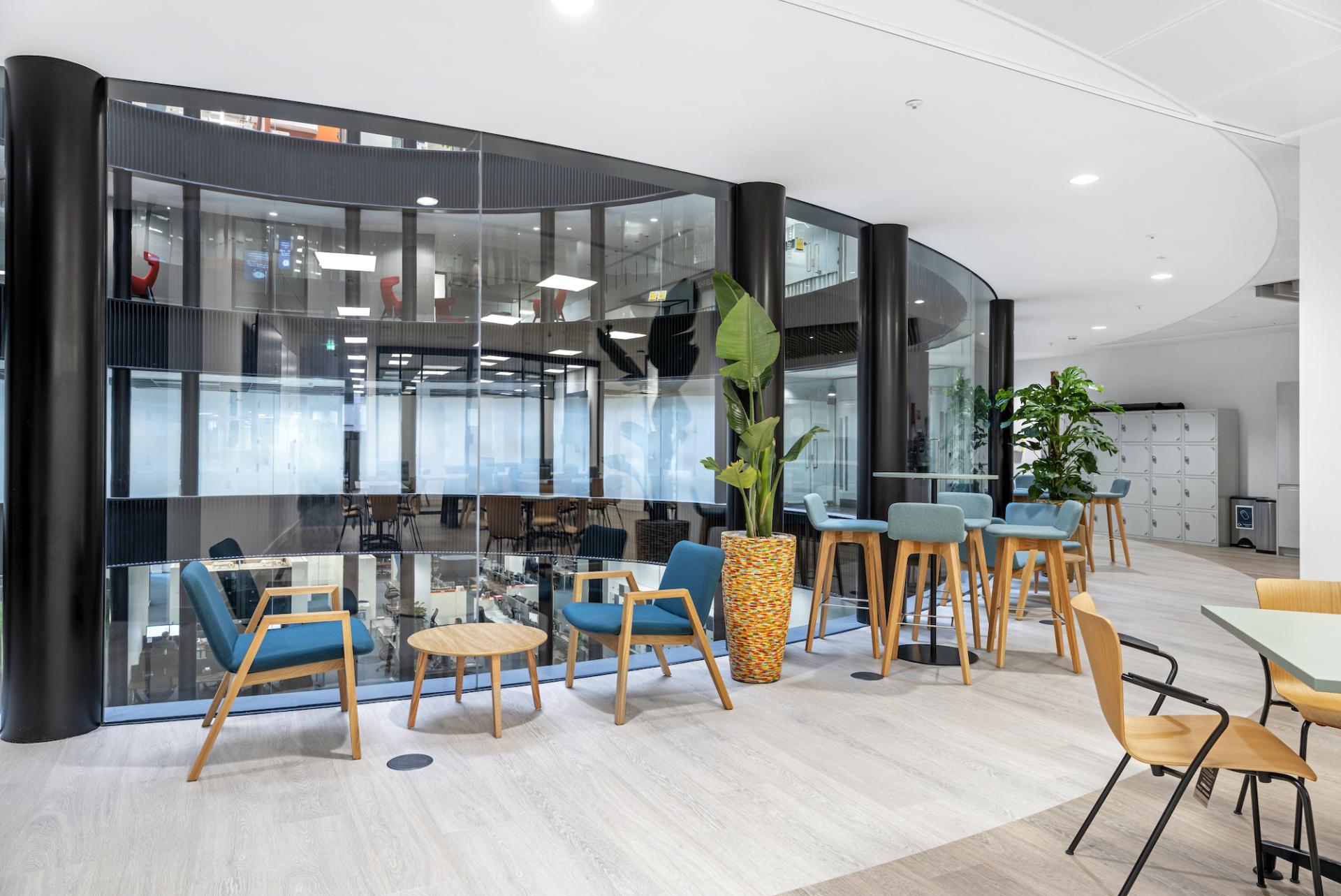 Modern office space featuring stylish seating, glass partitions, plants, and collaborative work areas, highlighting innovative workplace design.