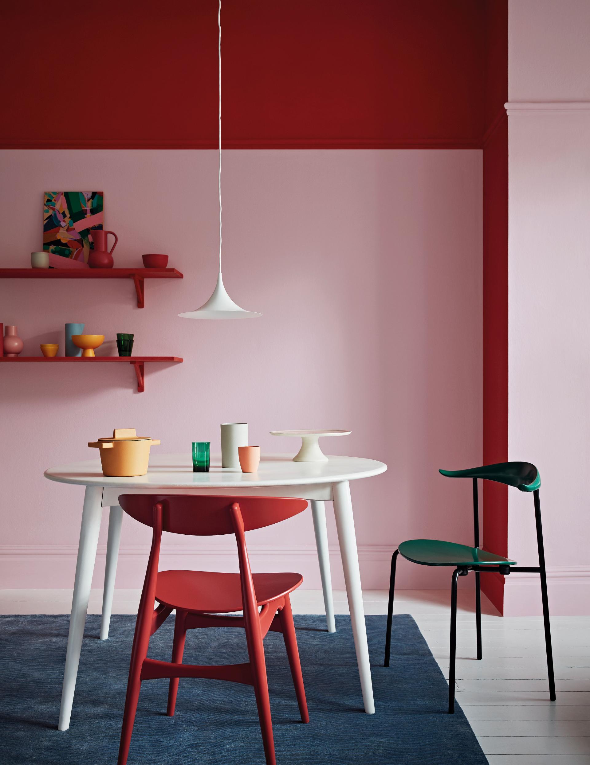 Stylish dining area featuring a round table, colorful chairs, and a vibrant red and pink wall for Spring/Summer decor.