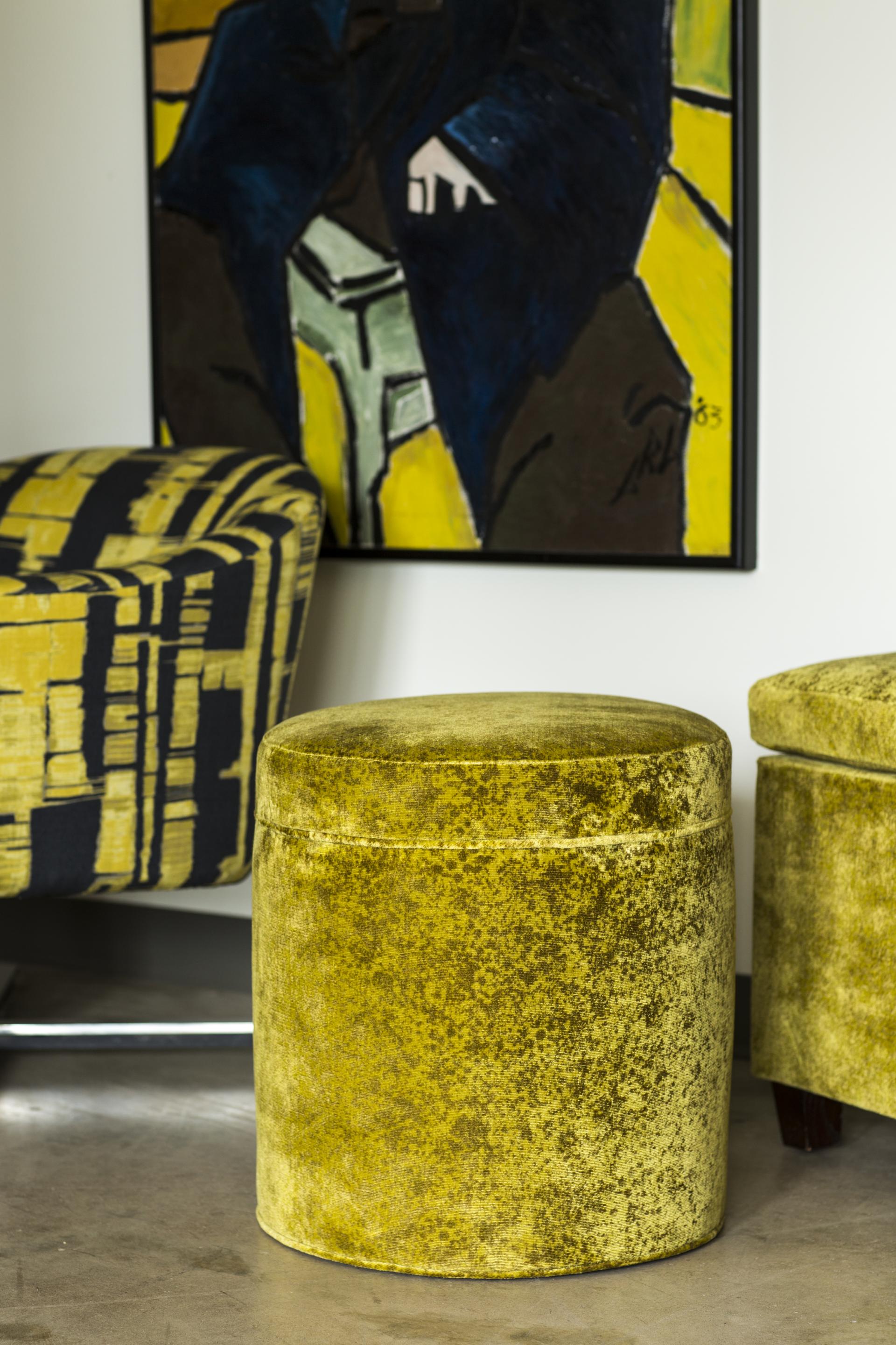 David Rockwell's new fabric collection features vibrant yellow upholstered stools and a colorful abstract painting in the background.