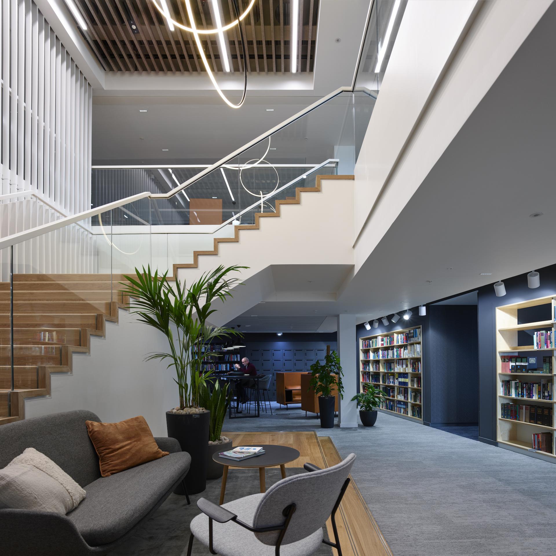 Modern workspace interior featuring a stylish staircase, lounge area, and bookshelves, emphasizing design and functionality in architecture.