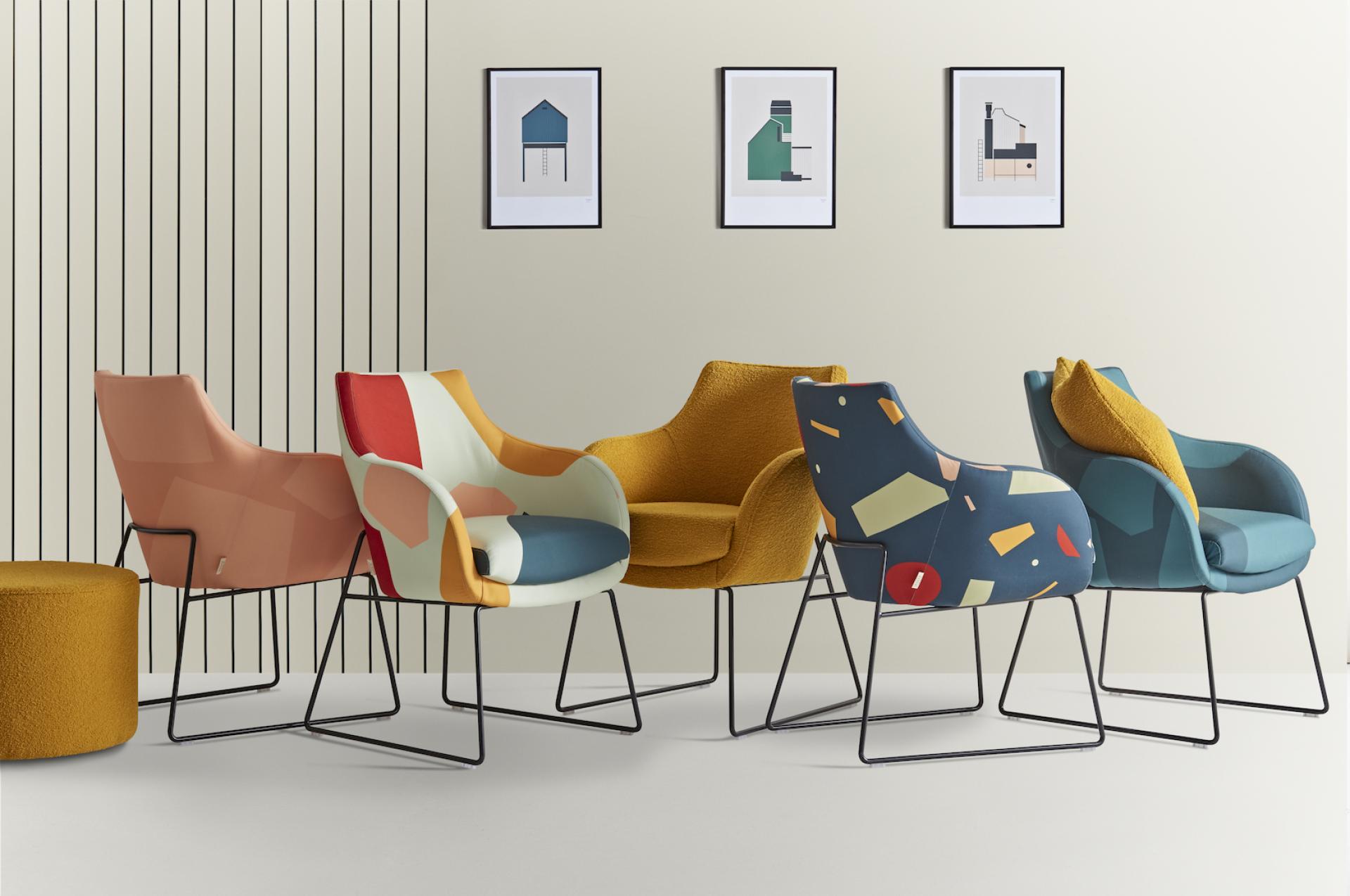 Colorful modern chairs with geometric patterns and a round pouf against a minimalist wall, showcasing Tom Pigeon’s design aesthetic.