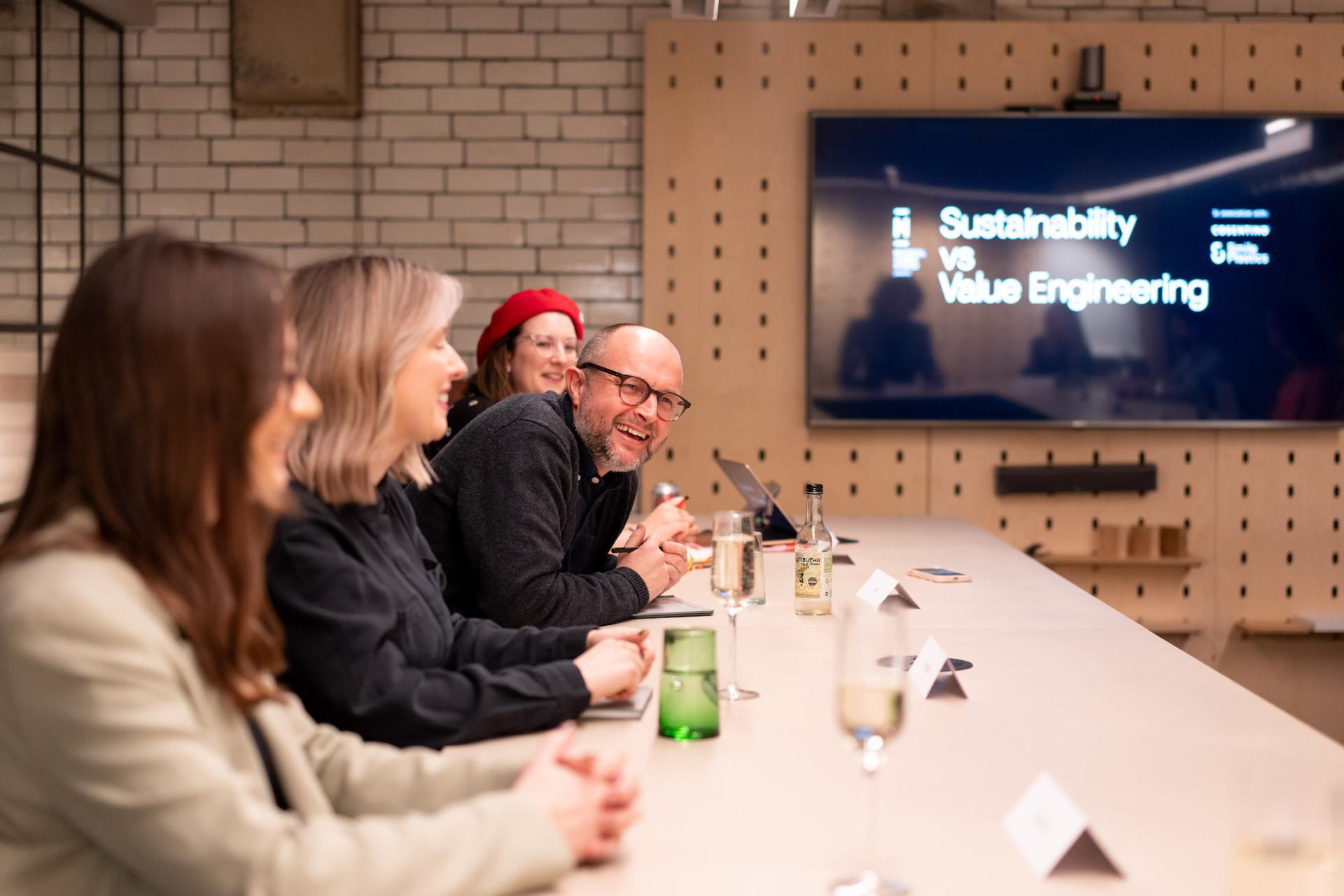 Panel discussion on sustainability and value engineering, featuring engaged participants and a presentation screen in a collaborative setting.