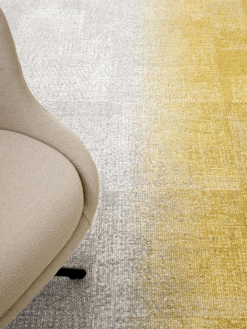 ReForm Transition carpet featuring a gradient of gray and yellow hues, accompanied by a modern beige chair.