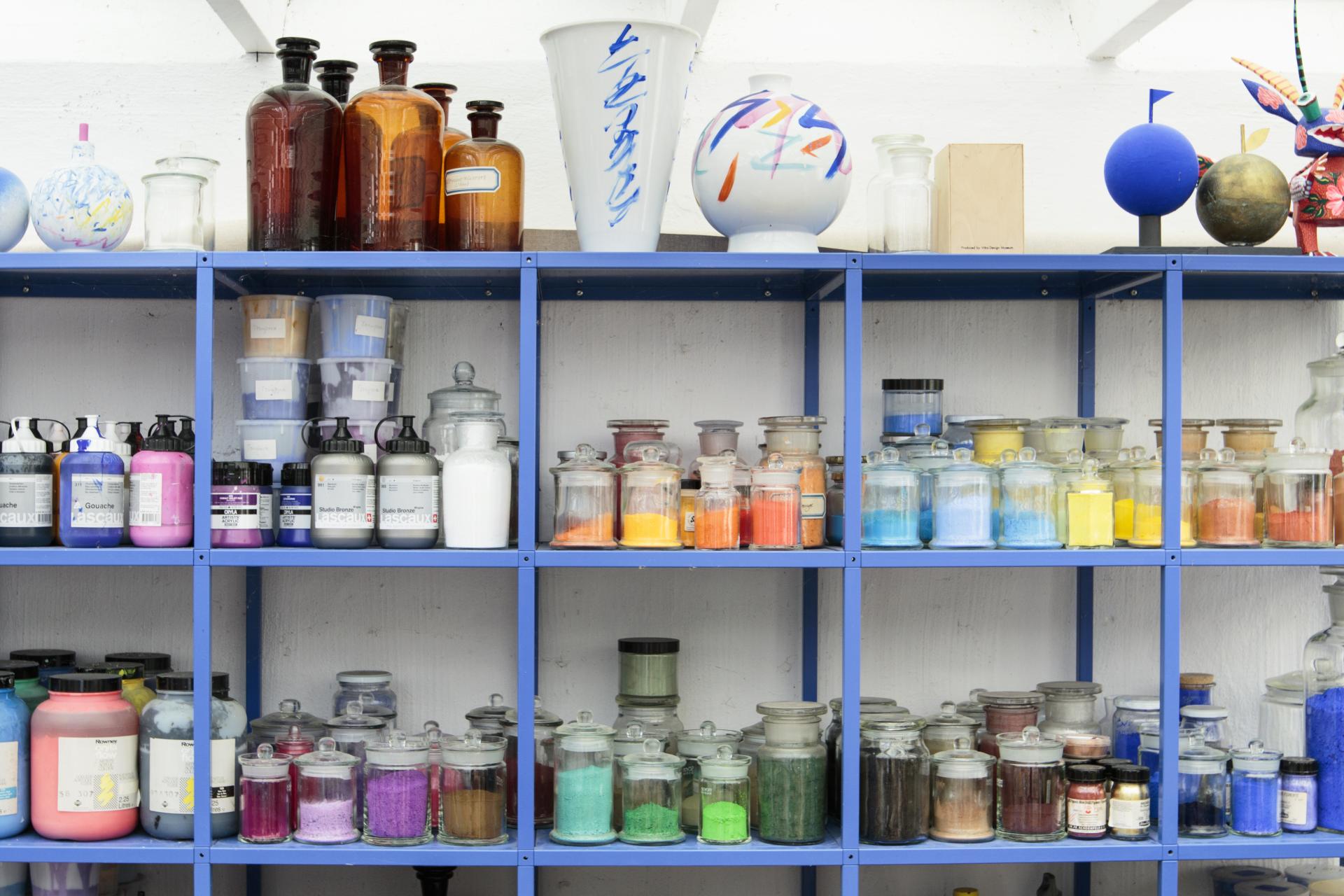 Shelves filled with colorful paints, powders, and glass jars, showcasing a vibrant array of artistic materials for design.