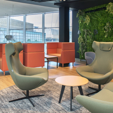 Vibrant lounge area at Alderley Park featuring green seating, orange partitions, and a living plant wall.