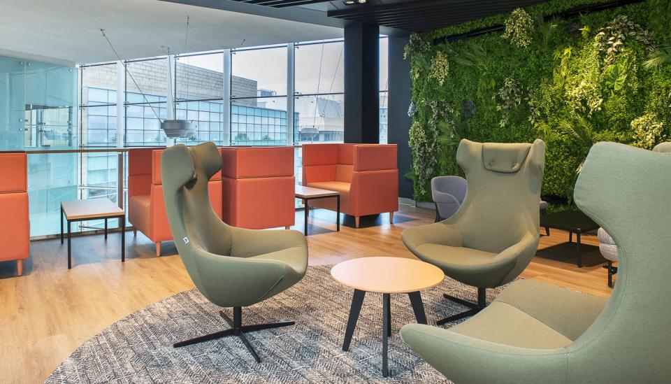 Vibrant lounge area at Alderley Park featuring green seating, orange partitions, and a living plant wall.