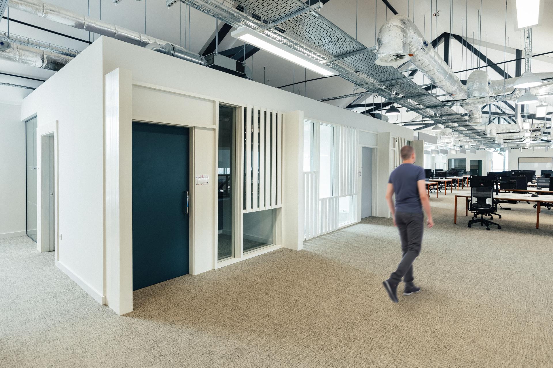 Modern office interior with open workspace, featuring white walls and a dark door, showcasing Crown Paints' vibrant finish.