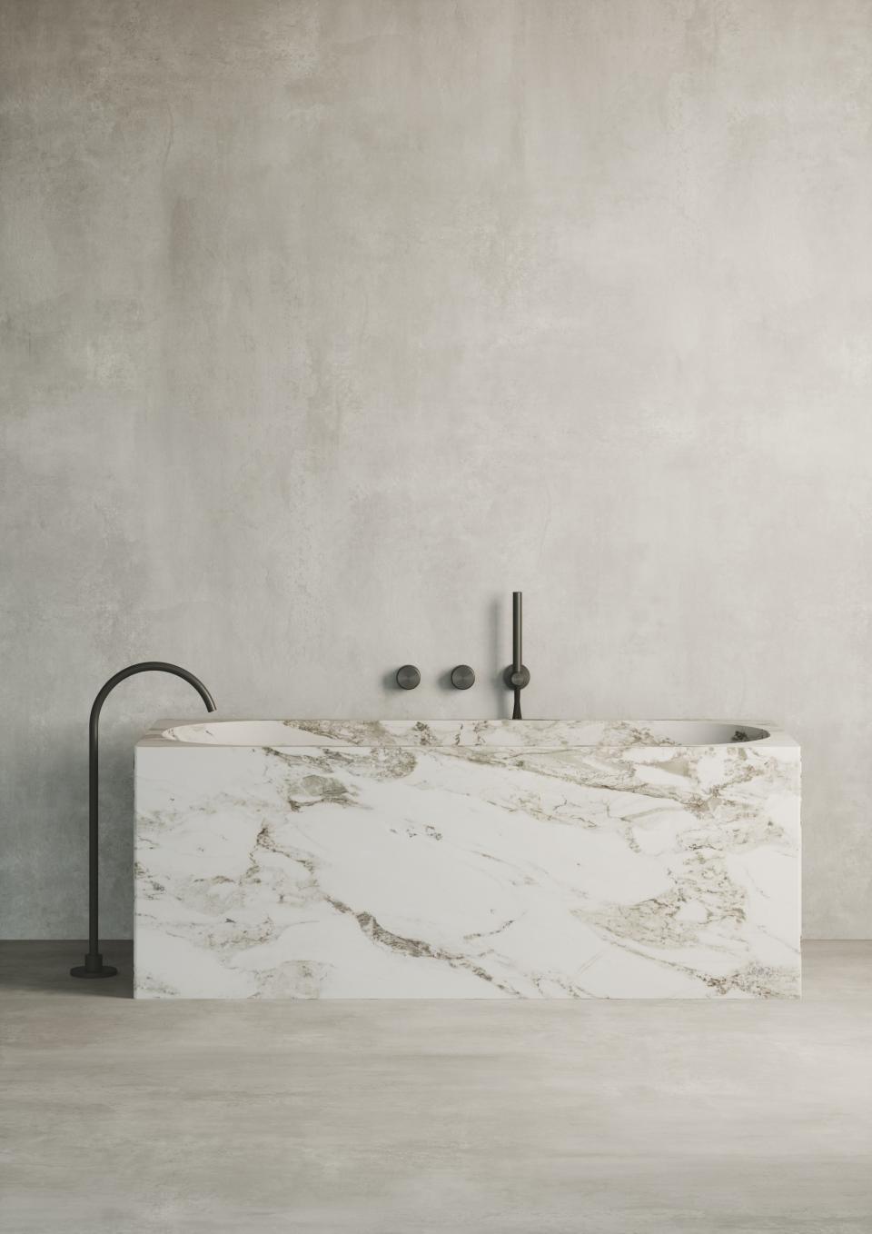 Sophisticated marble bathtub with sleek black fixtures against a minimalist concrete wall, showcasing Quadro Design Italy's new product line.