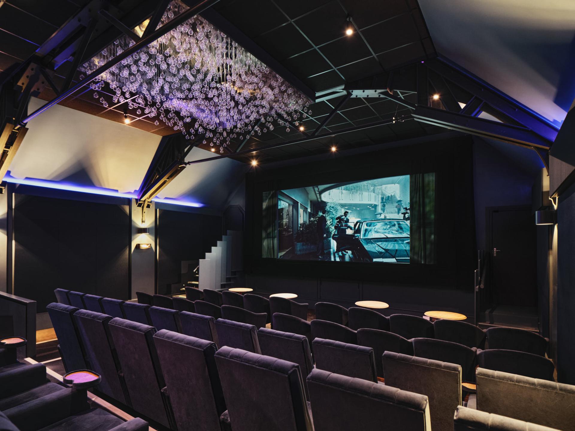 Modern cinema interior of The Lexi, showcasing plush seating, intricate lighting, and a large screen featuring a film.