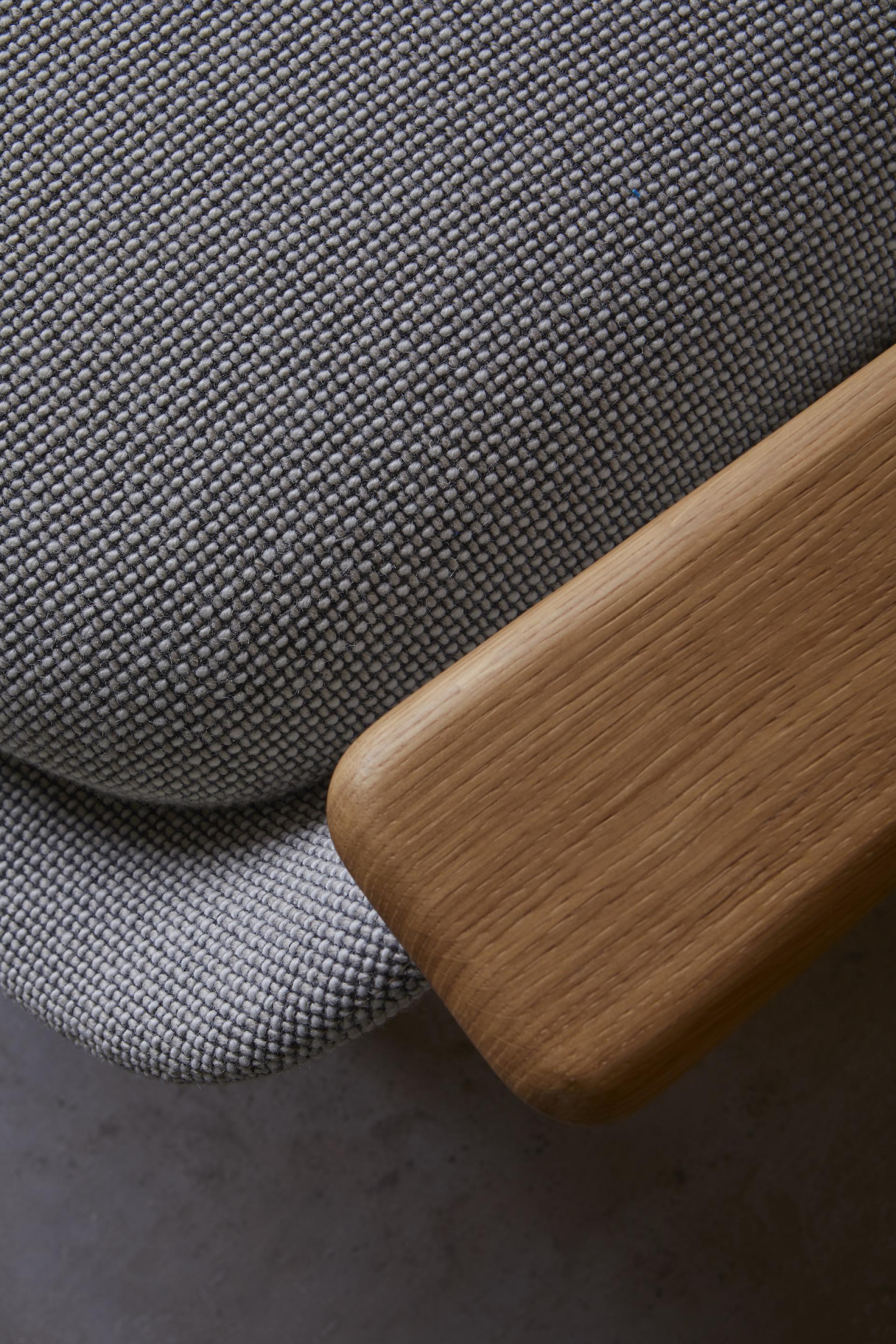 Textured grey fabric upholstery on a cozy chair, complemented by a smooth wooden armrest, highlighting sustainable design.