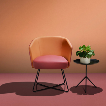 Stylish chair made with bio-based fabric, alongside a small table and potted plant, showcased at 100% Design.