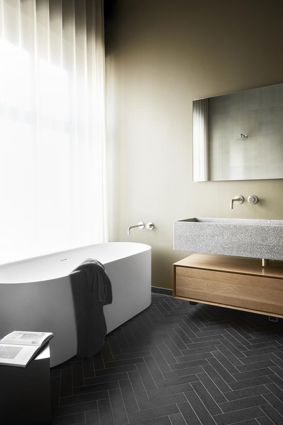Elegant bathroom featuring a freestanding tub, textured gray sink, and minimalist design elements by Emil Thorup.